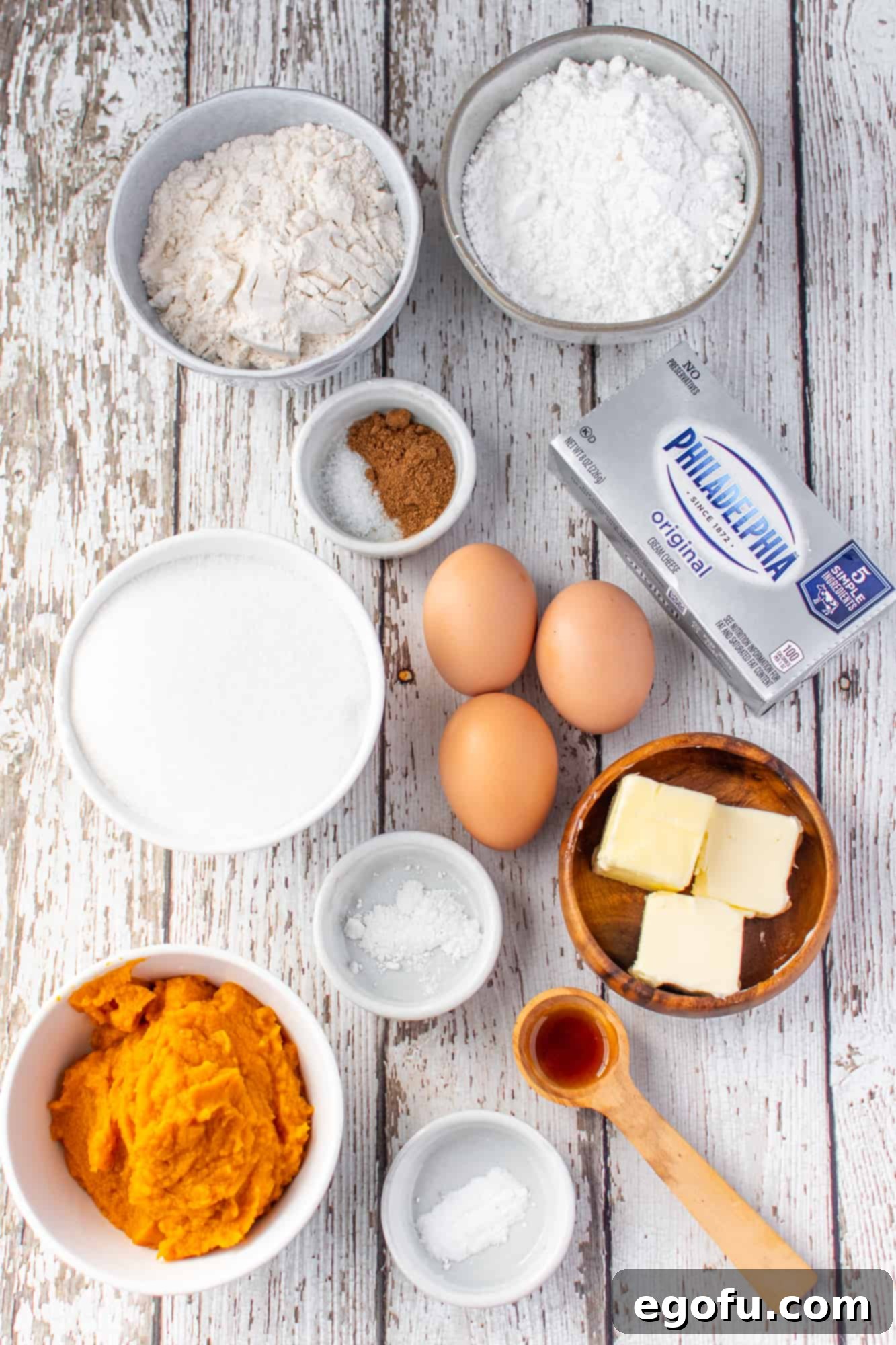 A collage of pumpkin roll ingredients: all-purpose flour, baking powder, baking soda, pumpkin pie spice, large eggs, white sugar, pure pumpkin, cream cheese, powdered sugar, butter, and vanilla extract.