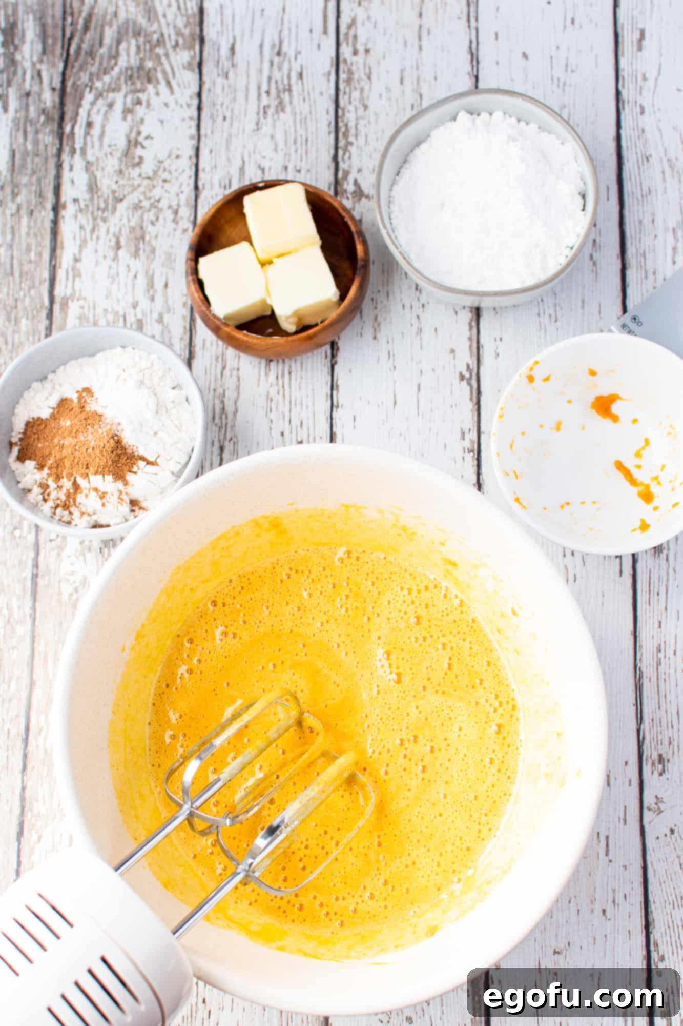 Pure pumpkin puree and vanilla extract being added to the creamy sugar and egg mixture in a white mixing bowl.