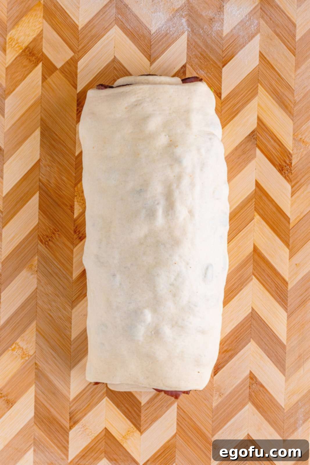 Philly Cheesesteak Pinwheels 12 rolled up cheesesteak log on a wooden cutting board.