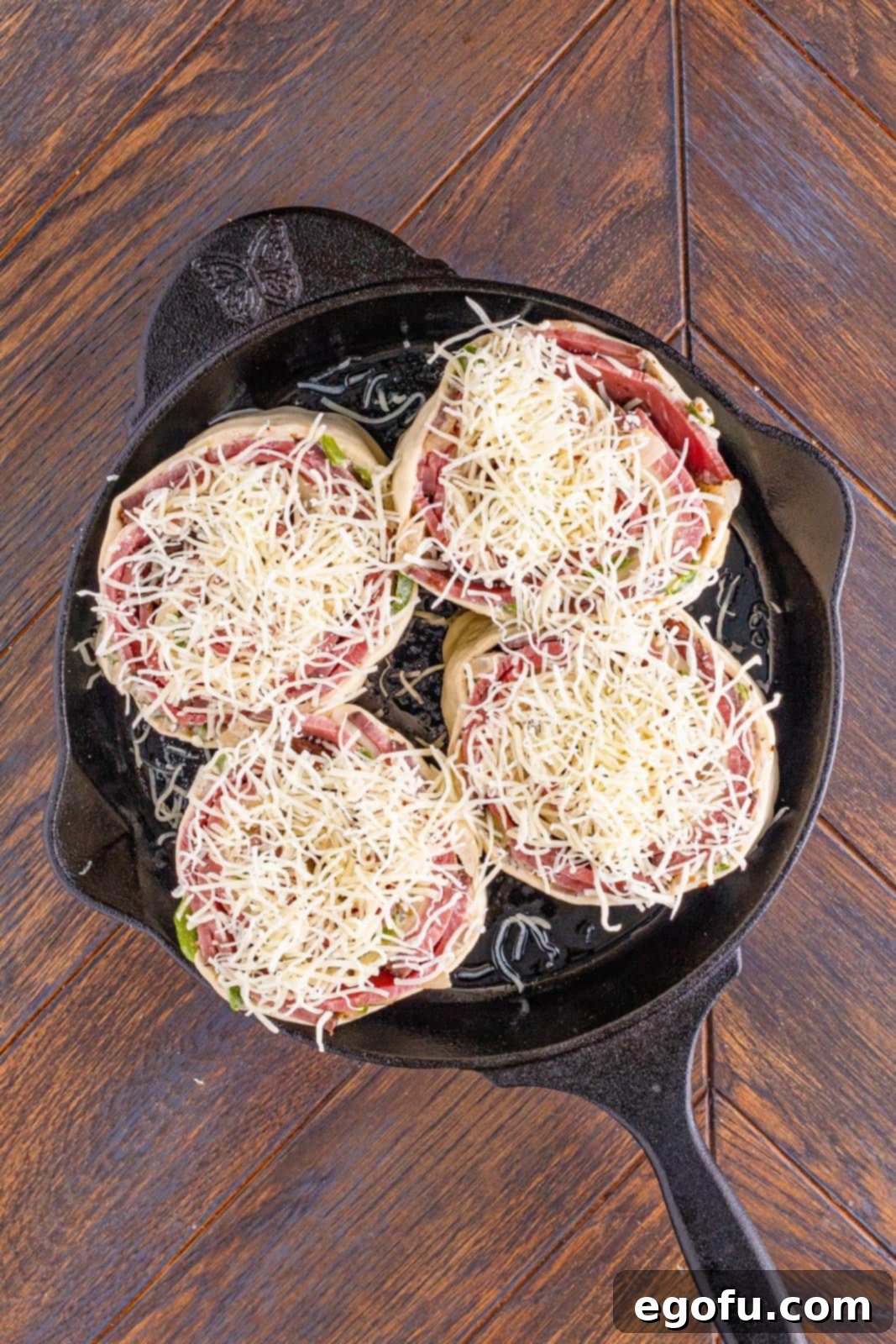 Philly Cheesesteak Pinwheels 15 shredded mozzarella cheese on roll ups in cast iron skillet.