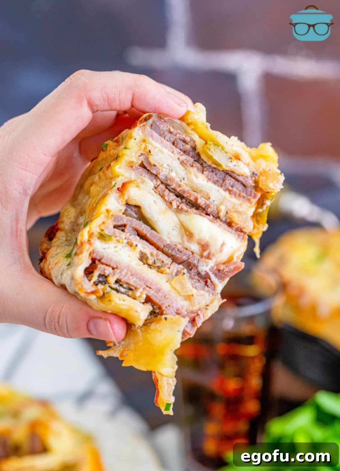 Philly Cheesesteak Pinwheels 17 hand holding up a Philly cheesesteak rollup.