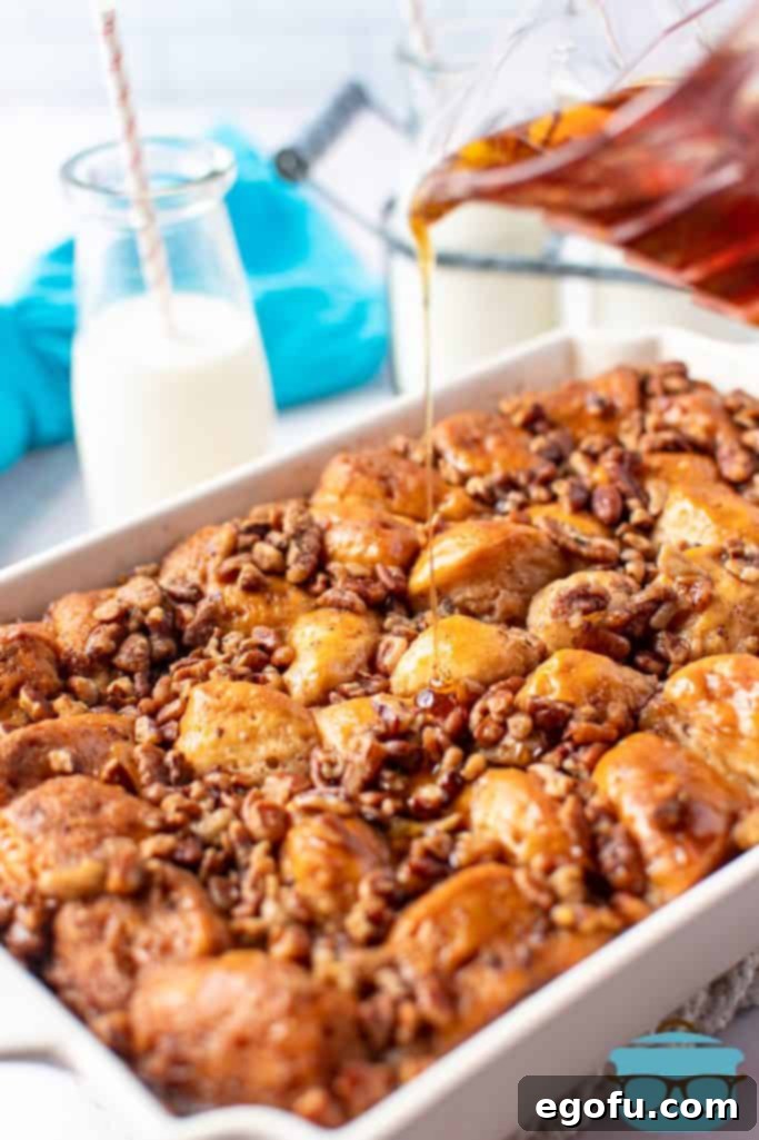Pouring maple syrup over a freshly baked French toast casserole with a golden pecan topping in a cream baking dish.