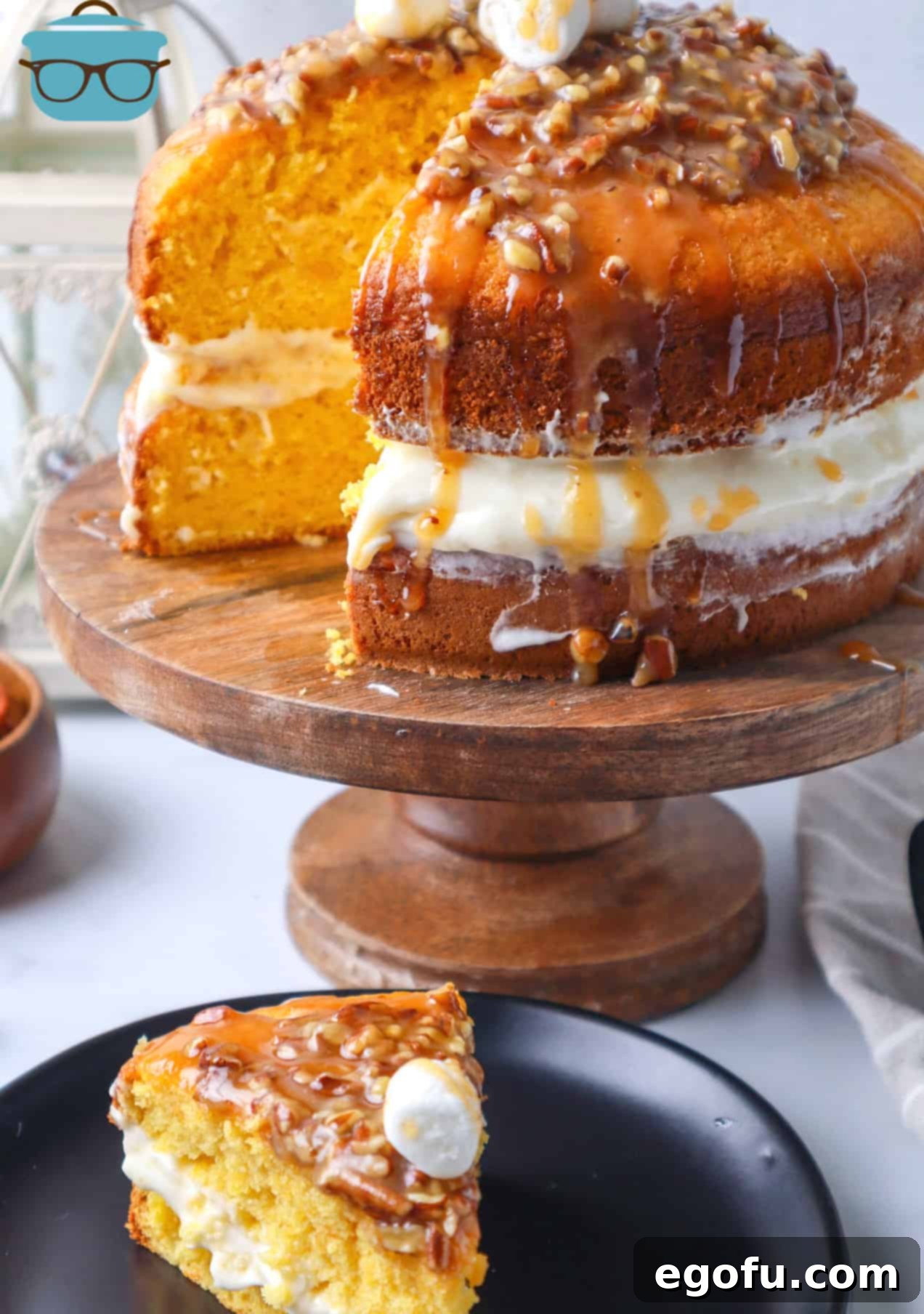 Effortless Sweet Potato Layer Cake 2 A slice of Loaded Sweet Potato Cake on a black plate, showcasing the distinct layers of cake and marshmallow fluff filling, topped with glistening candied pecans. The cake stands majestically on a wooden pedestal in the background.