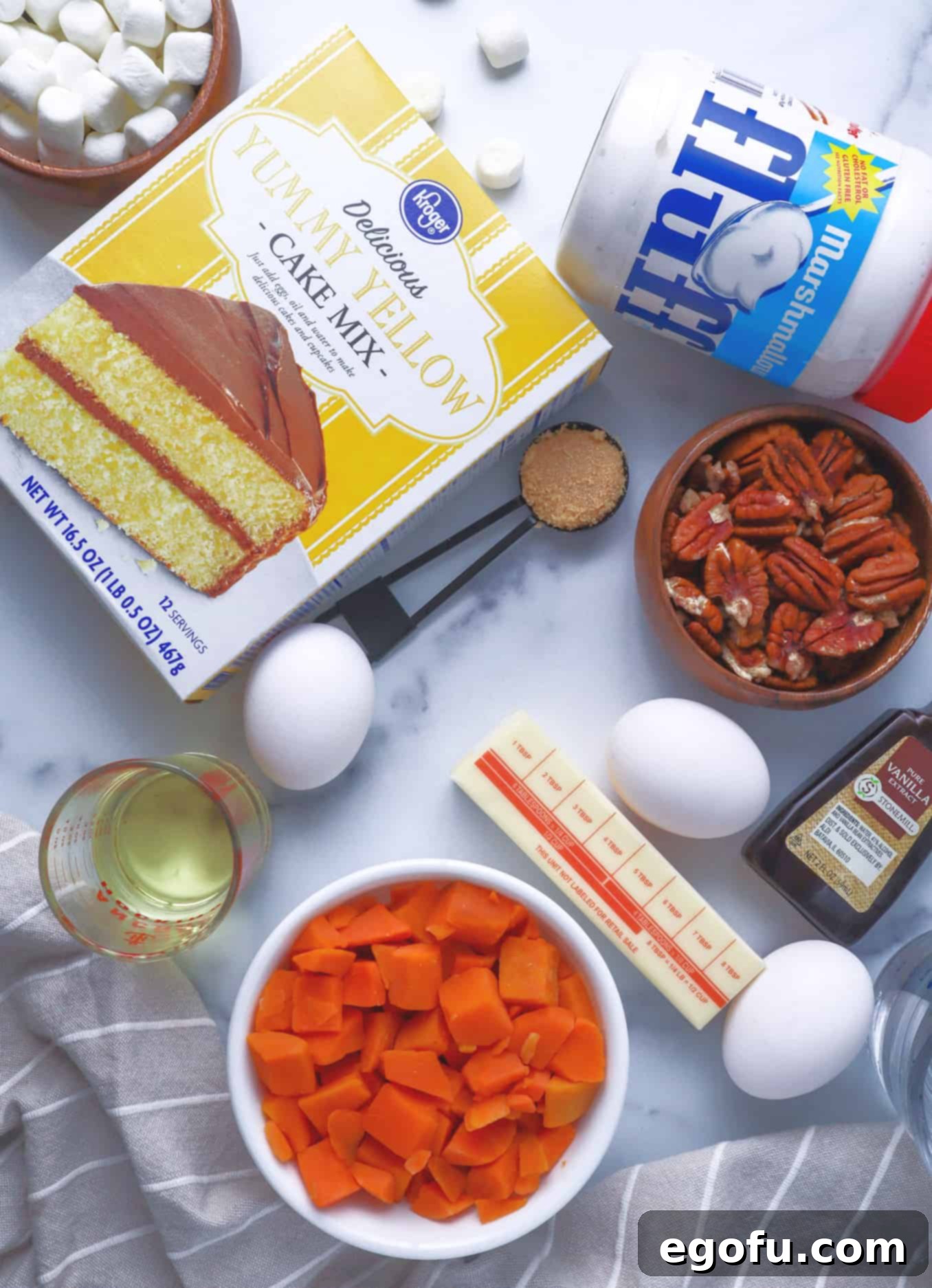 Effortless Sweet Potato Layer Cake 4 A flat lay photograph displaying all the essential ingredients for making the Layered Sweet Potato Cake: yellow cake mix, vegetable oil, large eggs, water, diced steamable sweet potato, marshmallow fluff, softened cream cheese, unsalted butter, light brown sugar, and chopped pecans.
