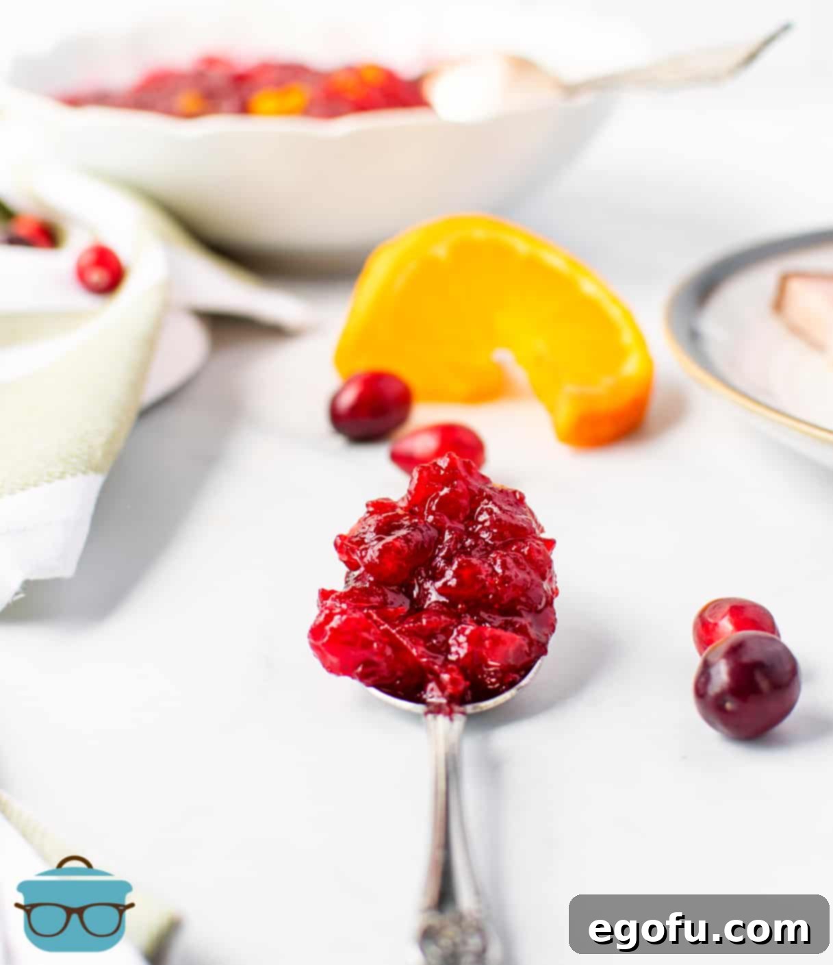 Effortless Cranberry Sauce 7 Cranberry sauce shown on a serving spoon on a white table with fresh cranberries scattered around.
