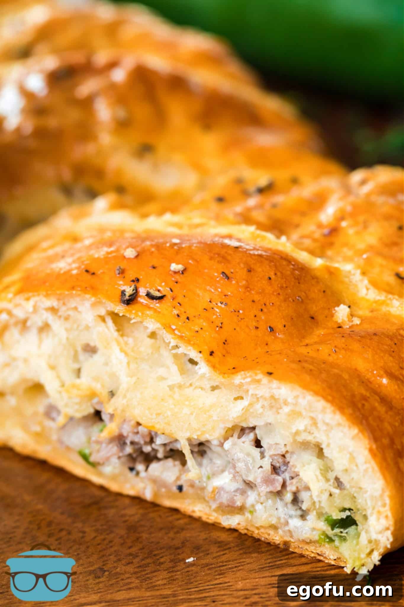 Golden-brown Sausage Crescent Ring with a slice removed, revealing the delicious sausage and cheese filling. Served on a dark wooden board.