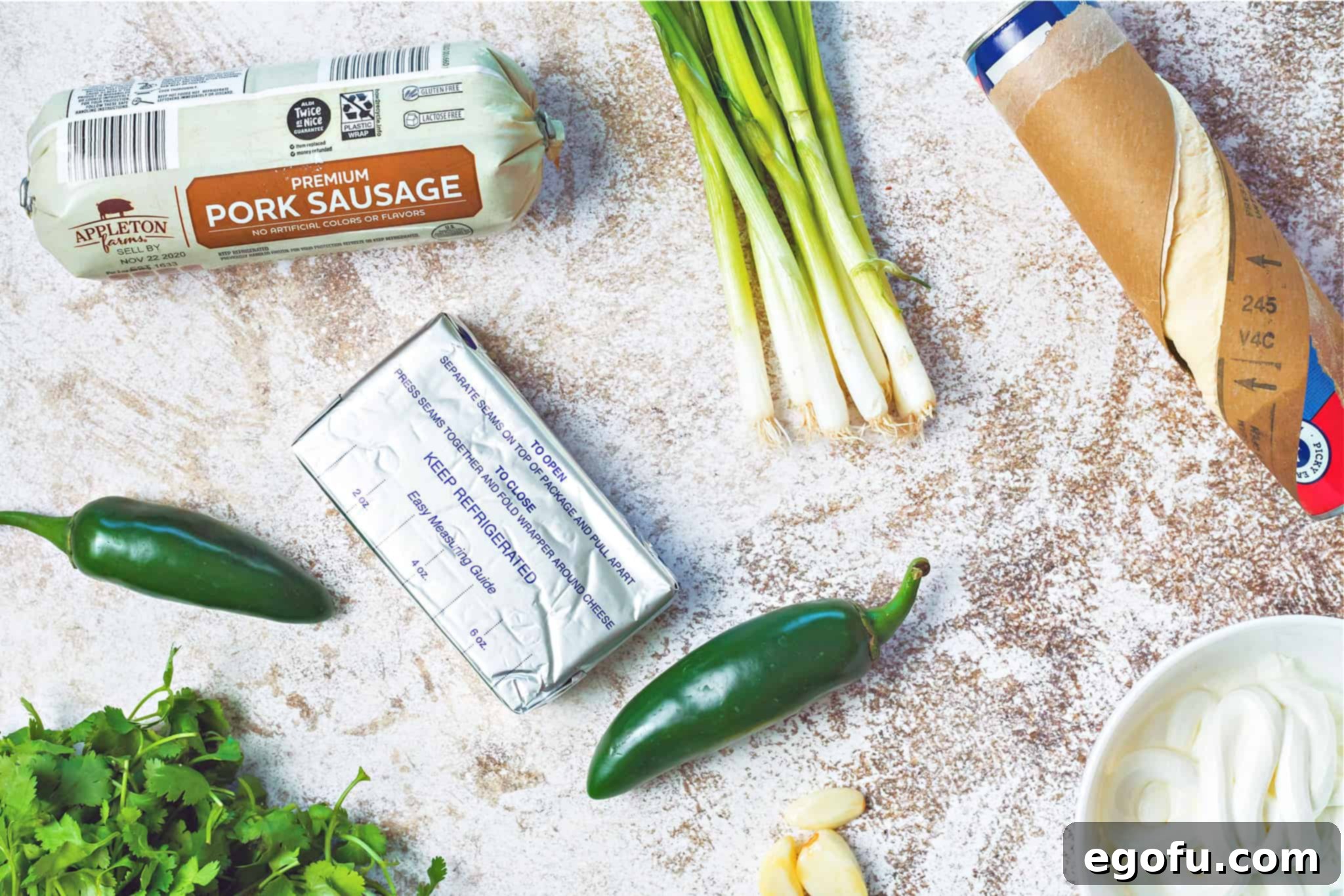 Array of fresh ingredients laid out for the Sausage Stuffed Crescent Ring and Green Onion Dip: cream cheese, ground pork sausage, vibrant green onions, diced jalapeños, fresh cilantro, and sour cream.