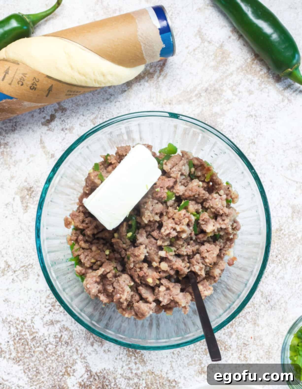 Cooked ground sausage mixed with softened cream cheese and diced jalapeños in a white mixing bowl, forming the savory filling for the crescent ring.