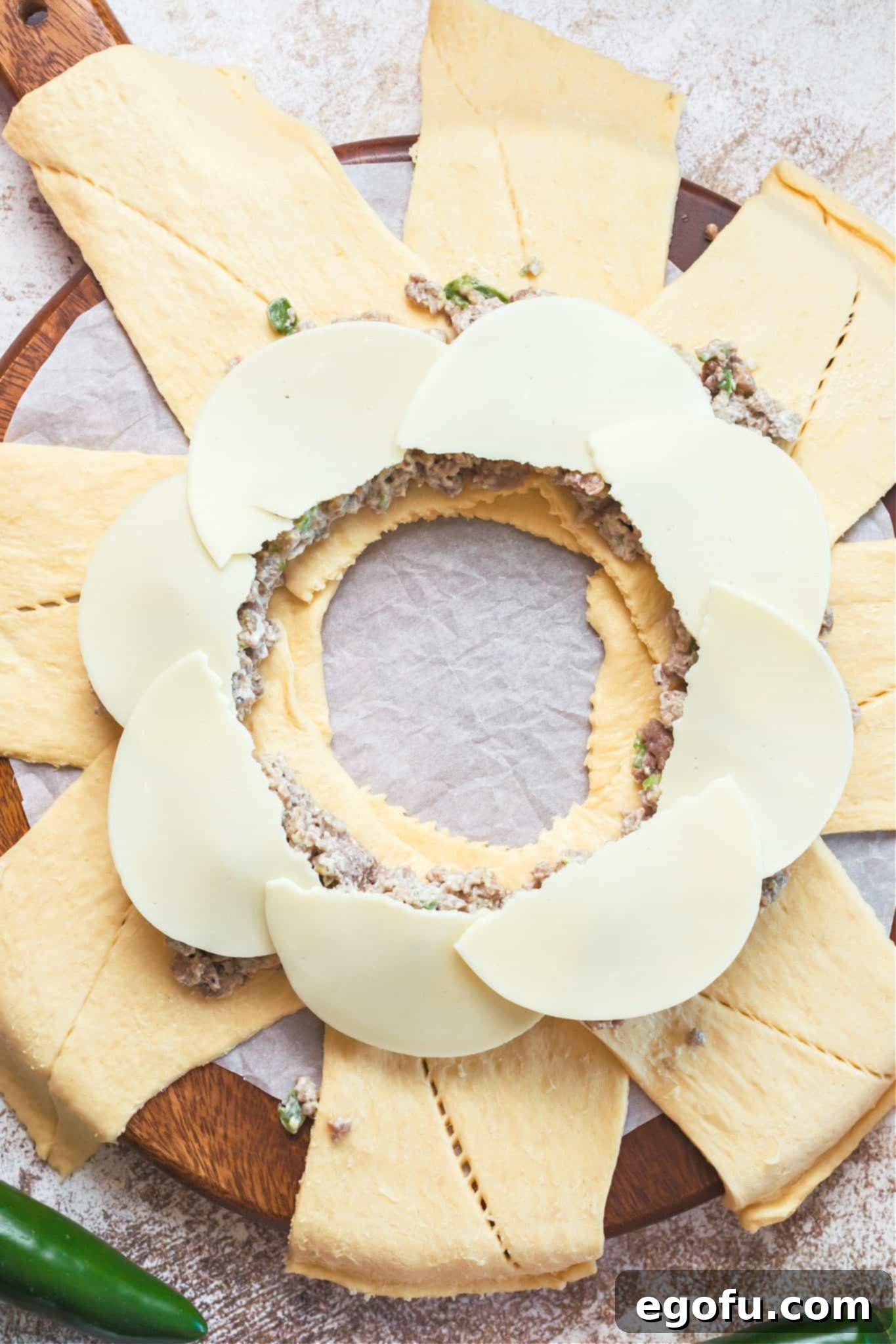 Half-slices of provolone cheese arranged on top of the sausage and cream cheese filling, covering the mixture before the crescent dough is folded.