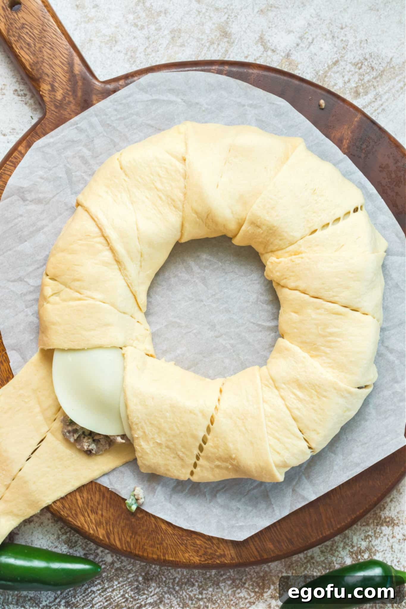 Crescent roll dough neatly wrapped around the sausage and cheese filling, forming a complete ring on parchment paper, ready for baking.