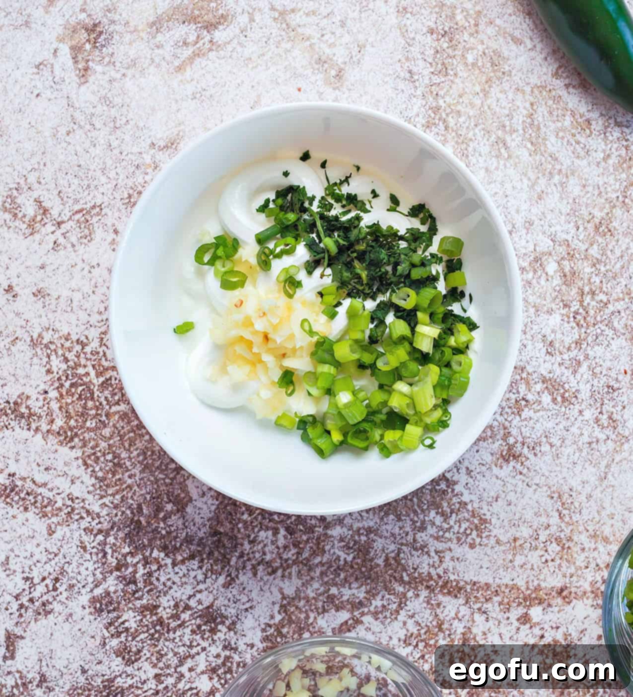 Fresh green onion, cilantro, and minced garlic mixed into creamy sour cream in a small white bowl, creating the vibrant dipping sauce.