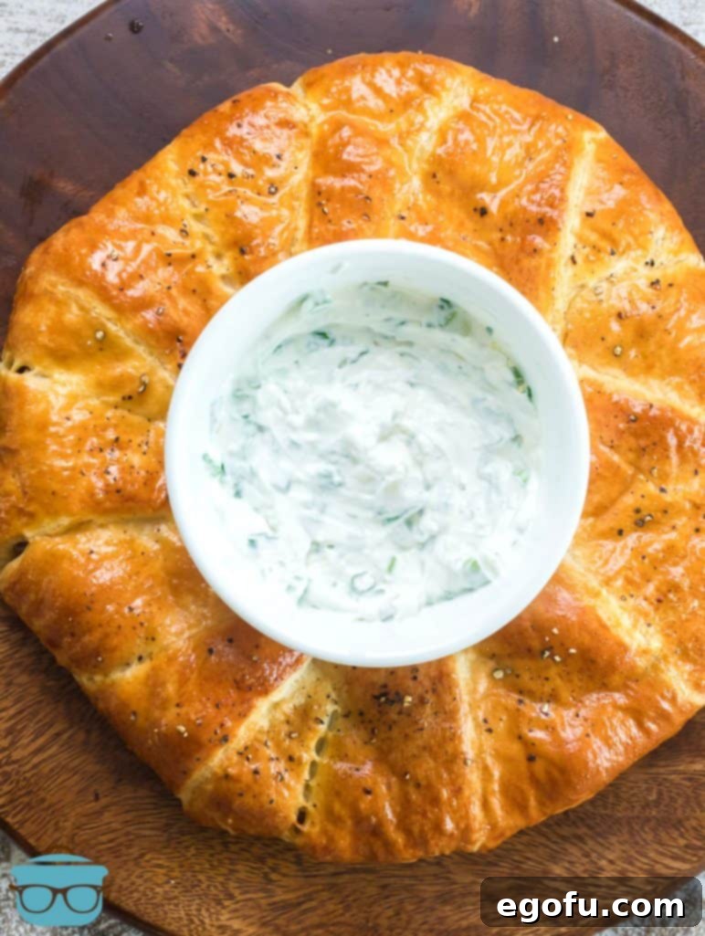 Beautifully baked Sausage Stuffed Crescent Ring presented on a serving platter, with a bowl of homemade green onion and garlic dip positioned in the center, ready to be enjoyed.