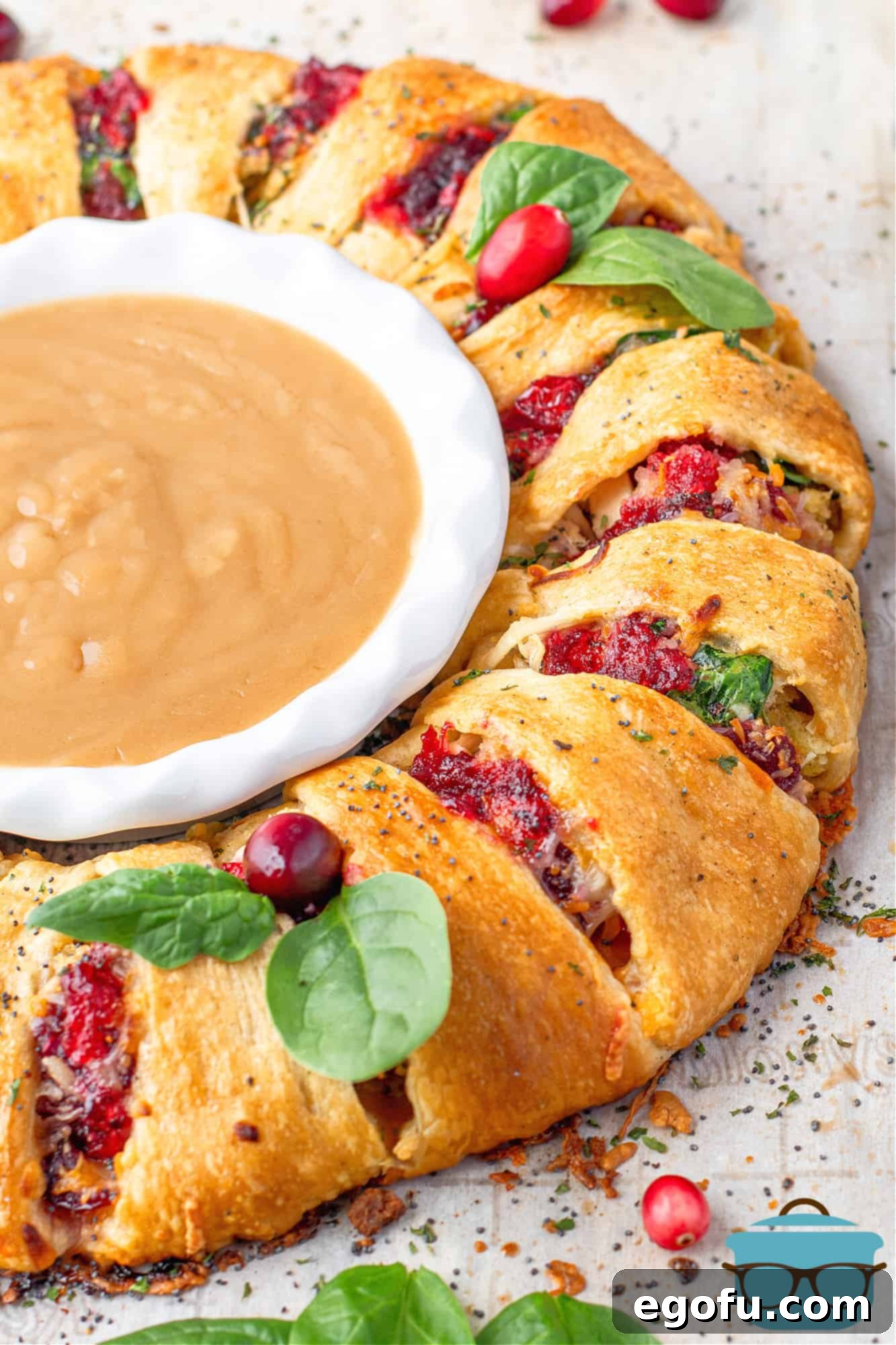 Festive Turkey Stuffing Crescent Bake 2 Fully baked leftover turkey and stuffing crescent ring, golden brown and garnished, shown with a white bowl of gravy in the center, ready to be served.