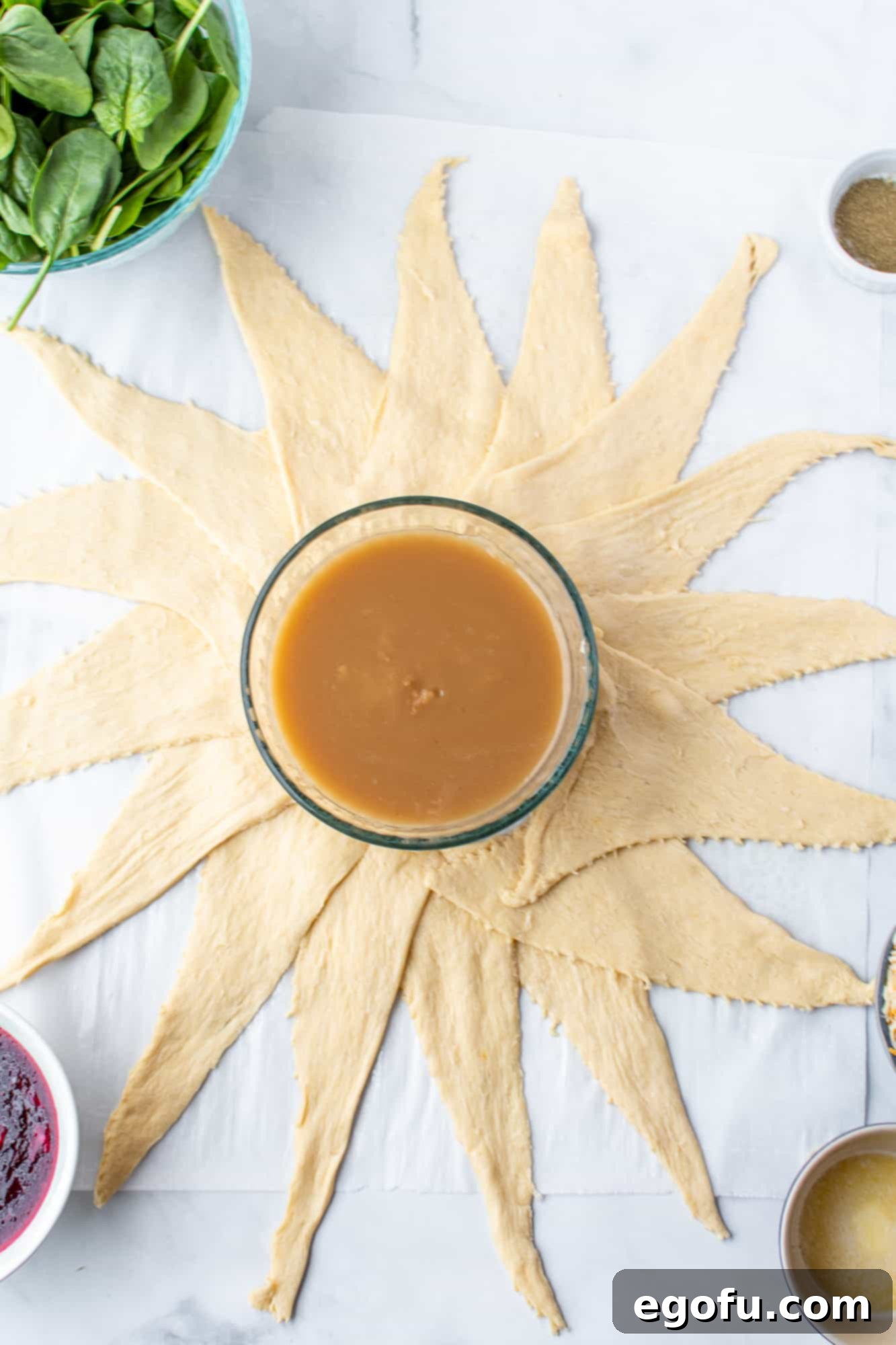 Festive Turkey Stuffing Crescent Bake 5 Crescent rolls laid out in a sunburst pattern on parchment paper around a central bowl, forming the base of the crescent ring.