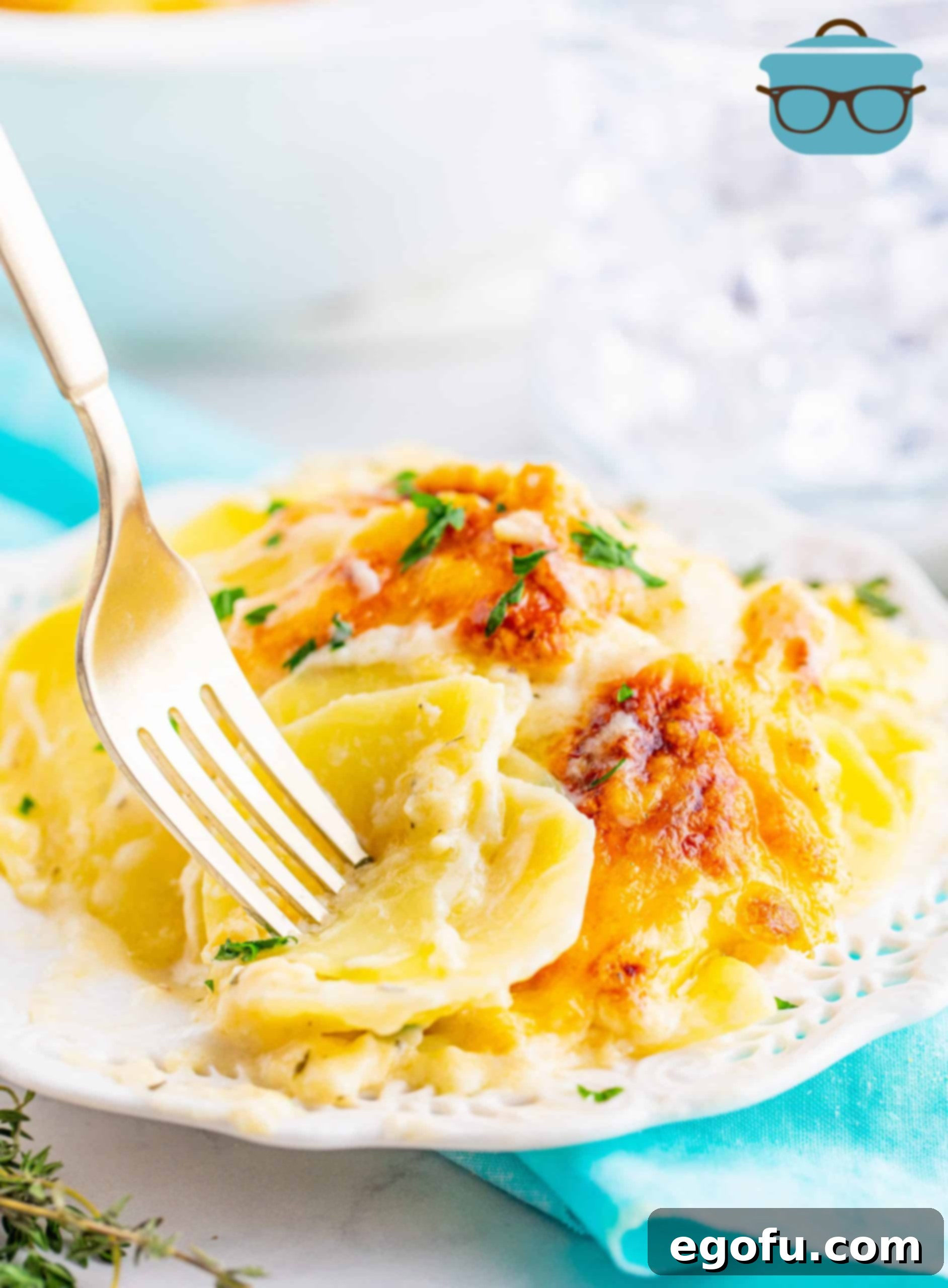 Scalloped Potatoes shown on a small white plate with a fork piercing several of the cooked potato slices.
