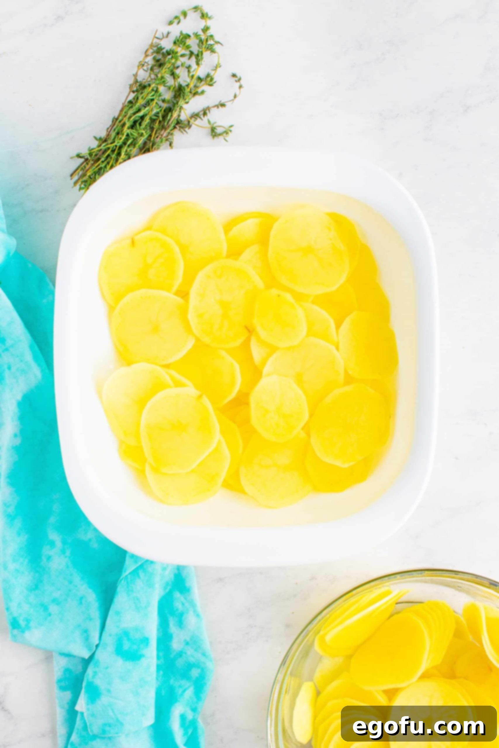 sliced gold potatoes in the bottom of a square, white baking dish.