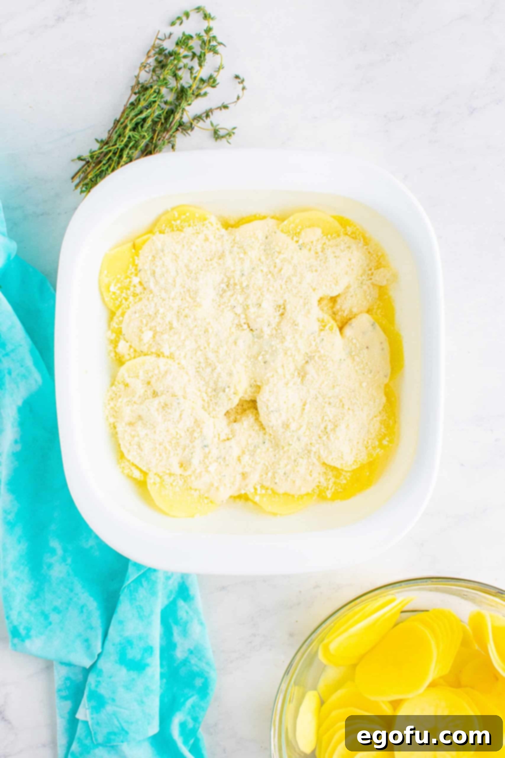 freshly grated Parmesan cheese sprinkled on top of cheese sauce and sliced potatoes in a white baking dish.