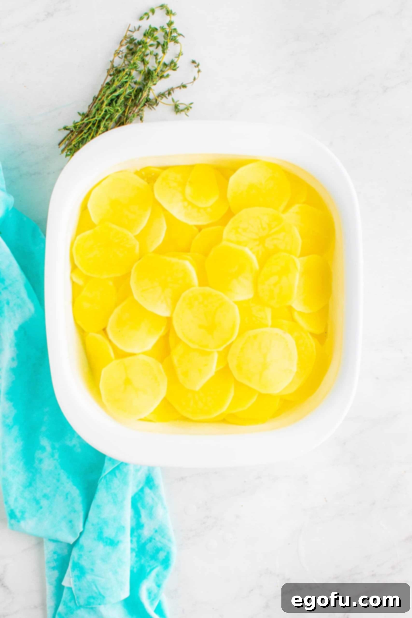 slice potatoes added in a layer on top of cheese inside a white, square baking dish.