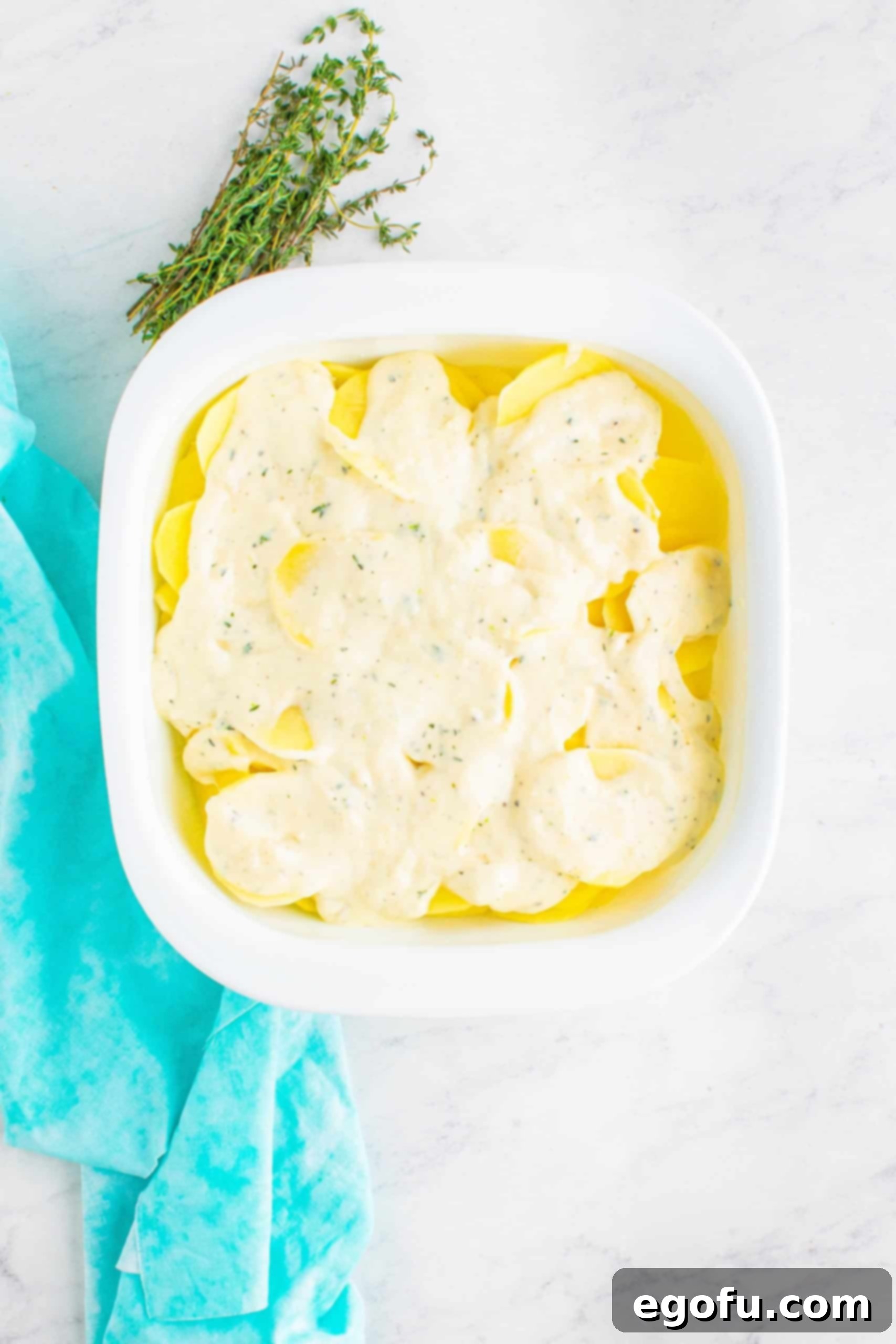 remaining gouda cheese sauce evenly layered on top of sliced potatoes in a square white baking dish.