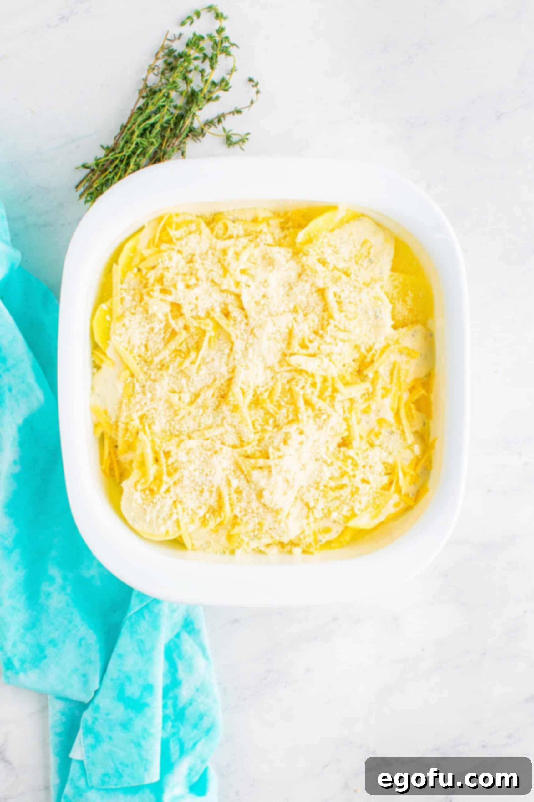 remaining shredded gouda and Parmesan cheeses sprinkled on top of cheese sauce and sliced potatoes in a square, white baking dish.
