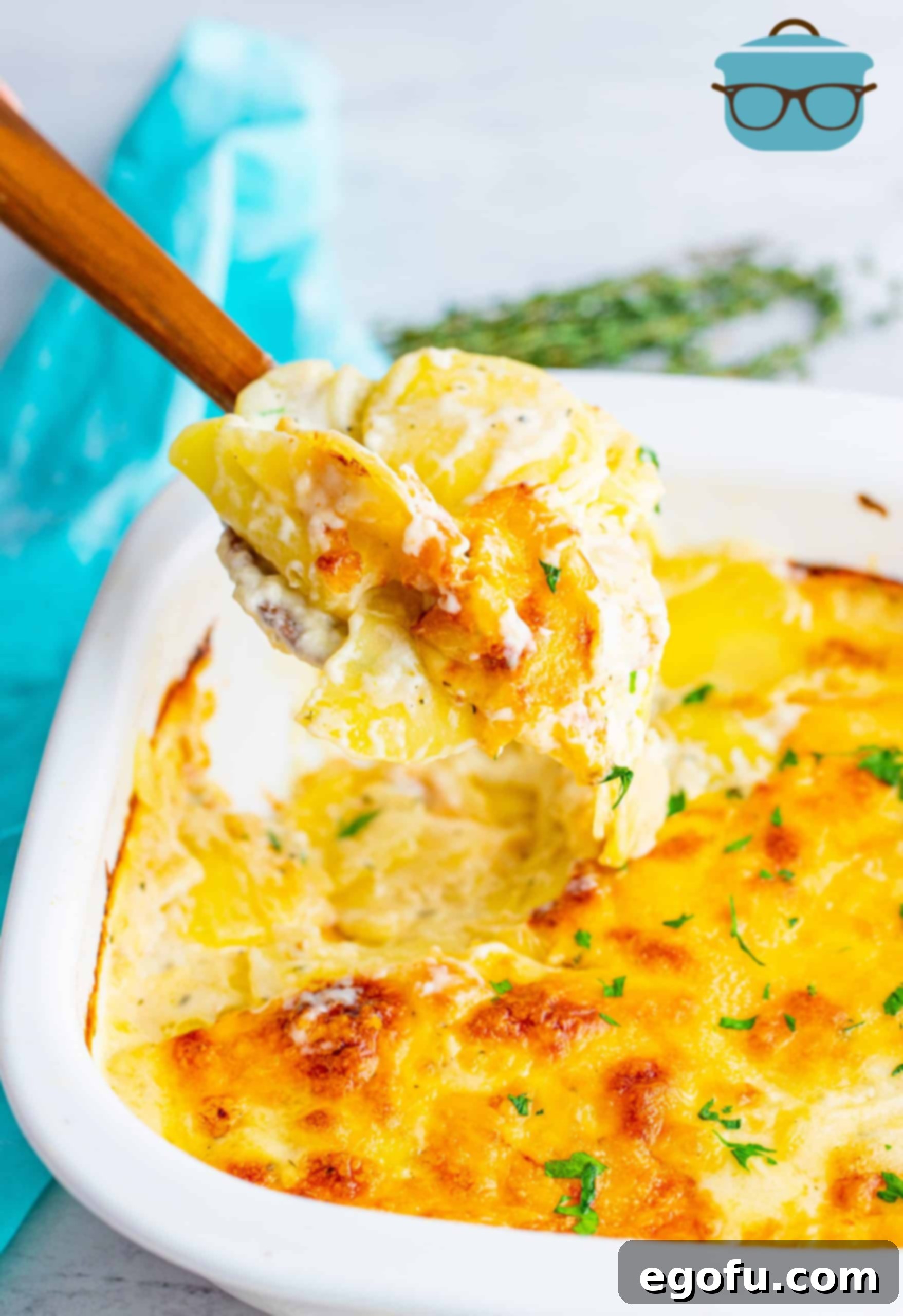 Cheesy Scalloped Potatoes, fully baked, shown in a white baking dish with a wooden spoon scooping out some of the potatoes.