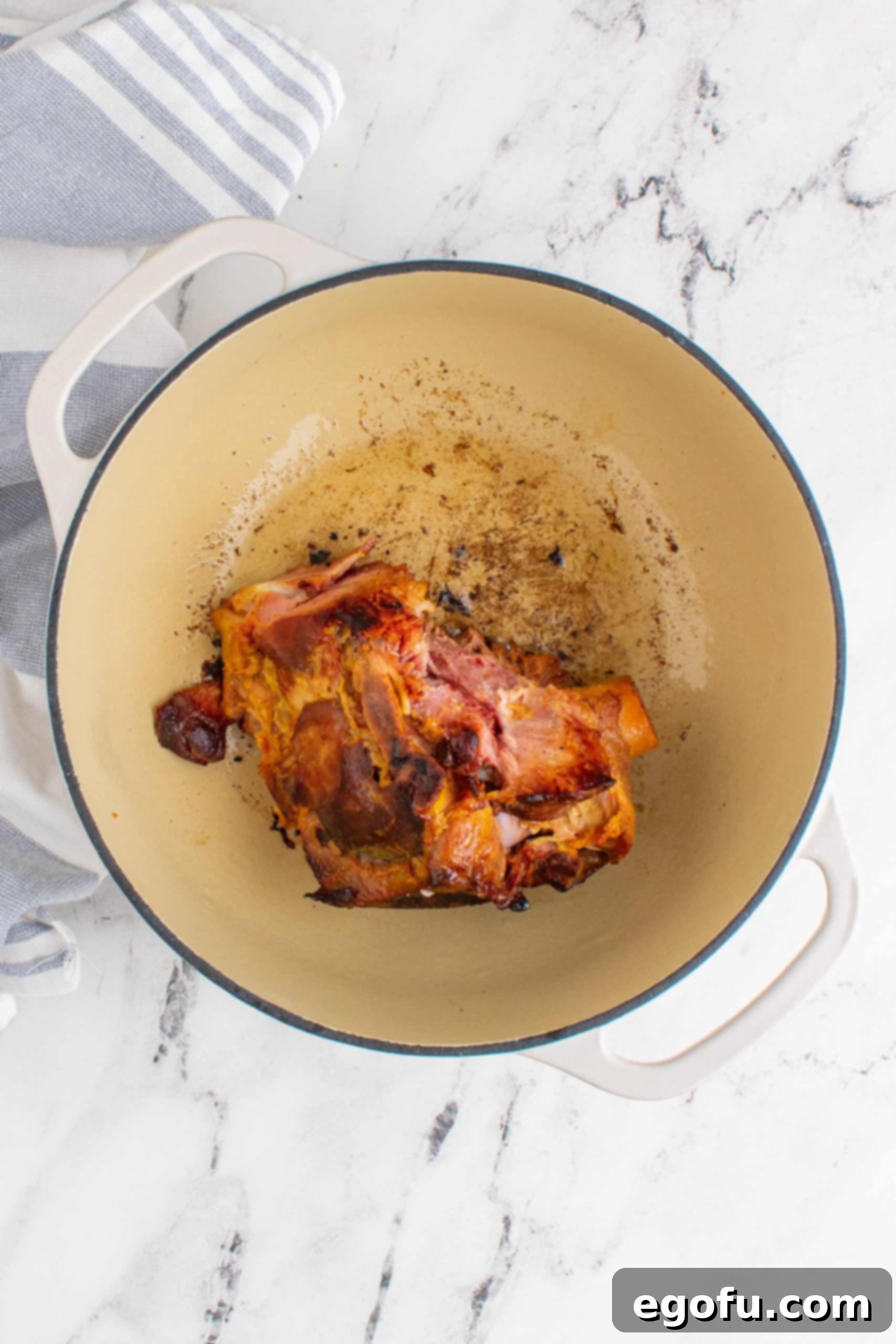 Ham bone browned on all sides in a white Dutch oven pot, creating a flavorful base for collard greens.