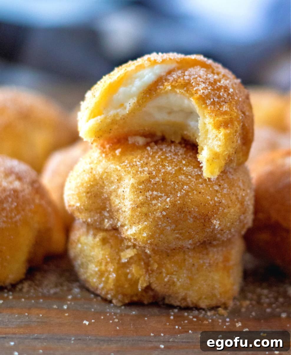 Air Fryer Pumpkin Spice Cream Cheese Bites shown stacked on a wooden surface with a bite taken out of the top cream cheese ball.