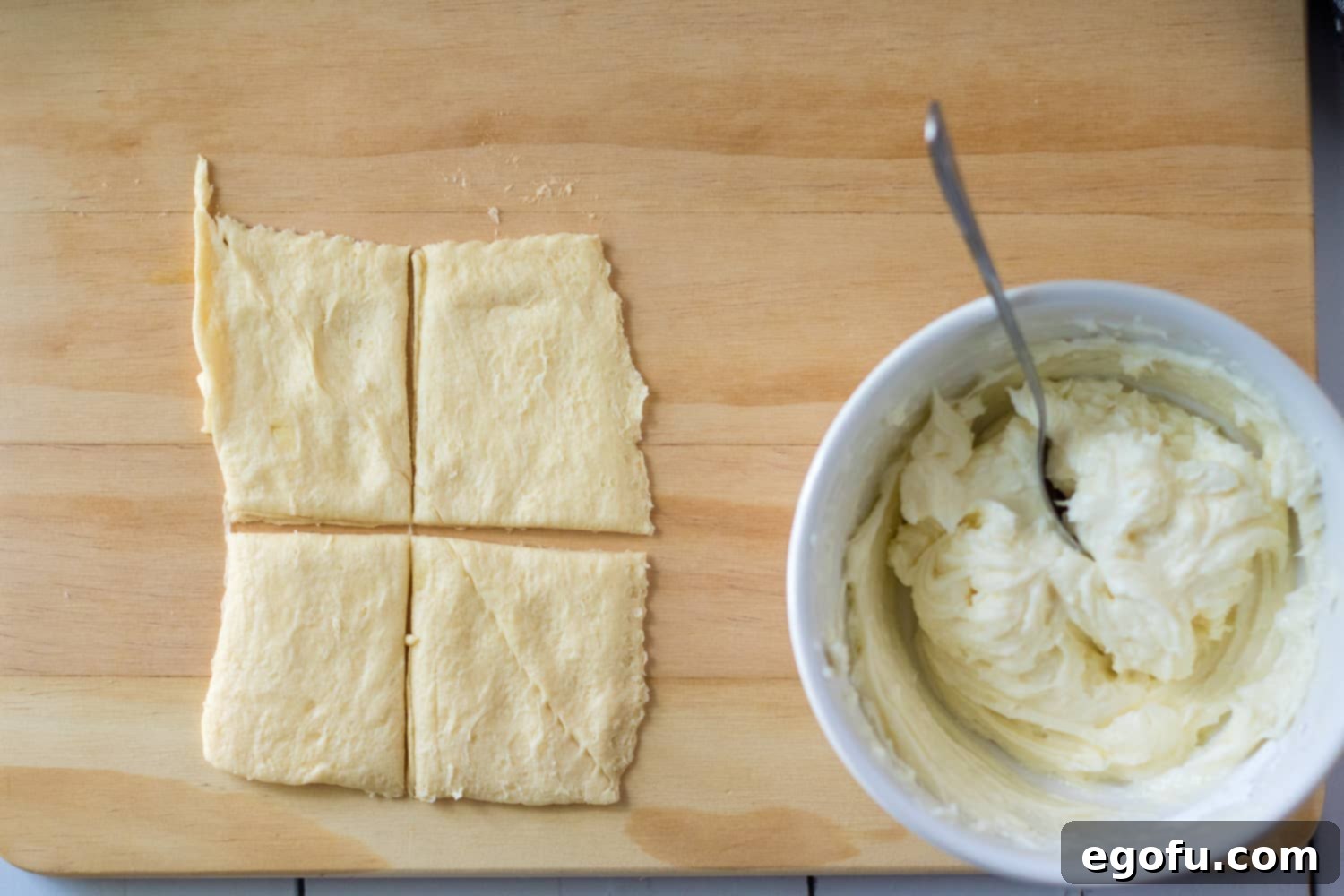 crescent roll dough made into four squares with a bowl of sweetened cream cheese off to the right side.