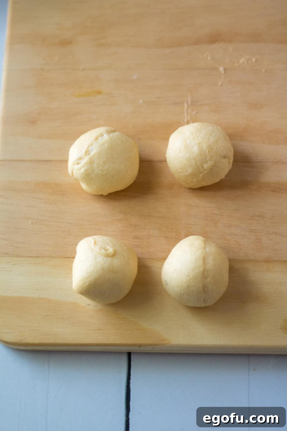 crescent roll dough wrapped around cream cheese shaped into balls on a wooden cutting board.
