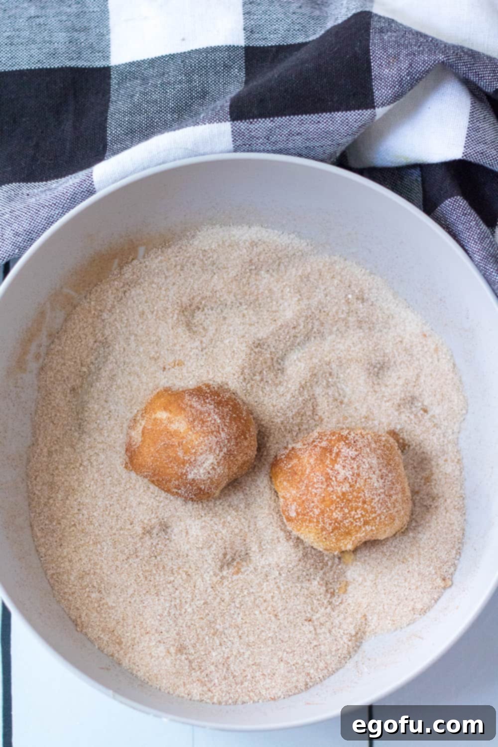 rolling air fried dough balls in pumpkin spice and cinnamon sugar mixture in a white bowl.