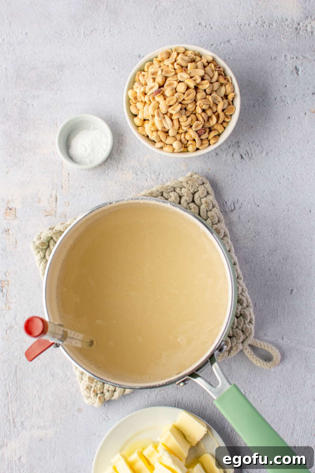 Golden Crunch Peanut Brittle 5 Sugar, water, corn syrup, and salt melting together in a medium saucepan, with a candy thermometer clipped to the side.