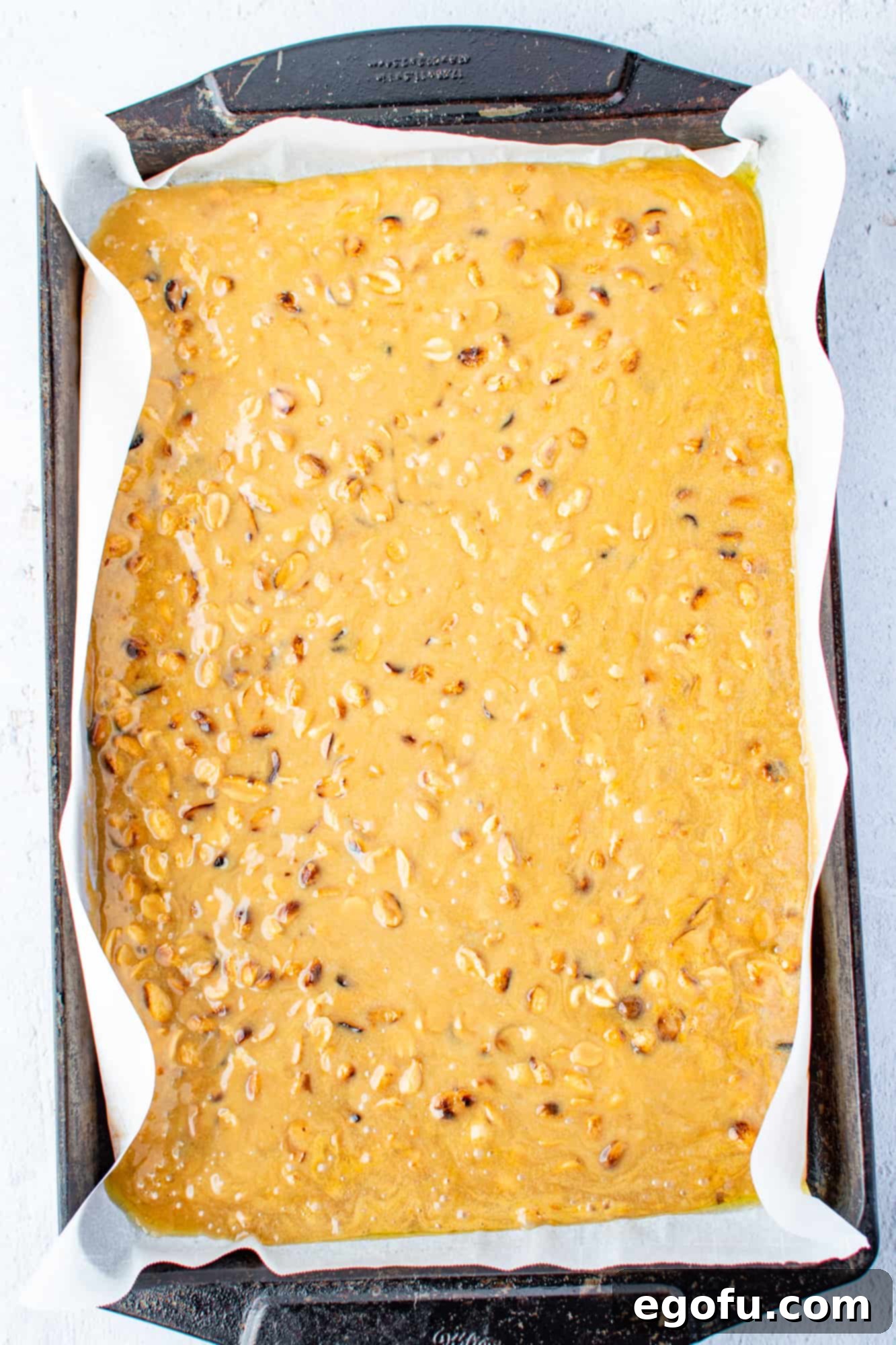 Golden Crunch Peanut Brittle 9 Liquid peanut brittle freshly poured onto a parchment paper-lined cookie sheet, being smoothed out to a thin, even layer.