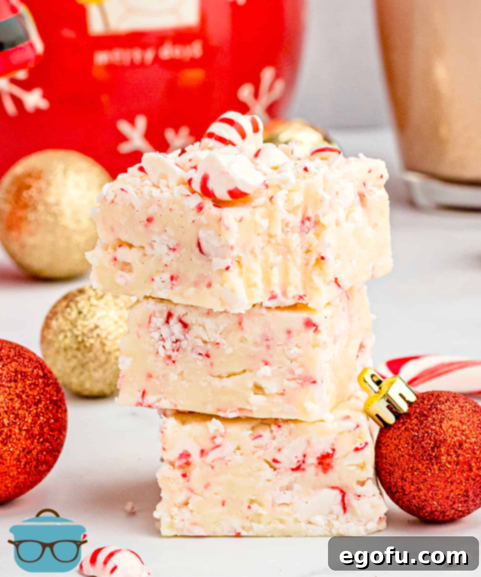 Delicious peppermint fudge pieces stacked high on a elegant marble surface, with a cozy cup of hot chocolate blurred in the background, creating a warm and inviting holiday scene.