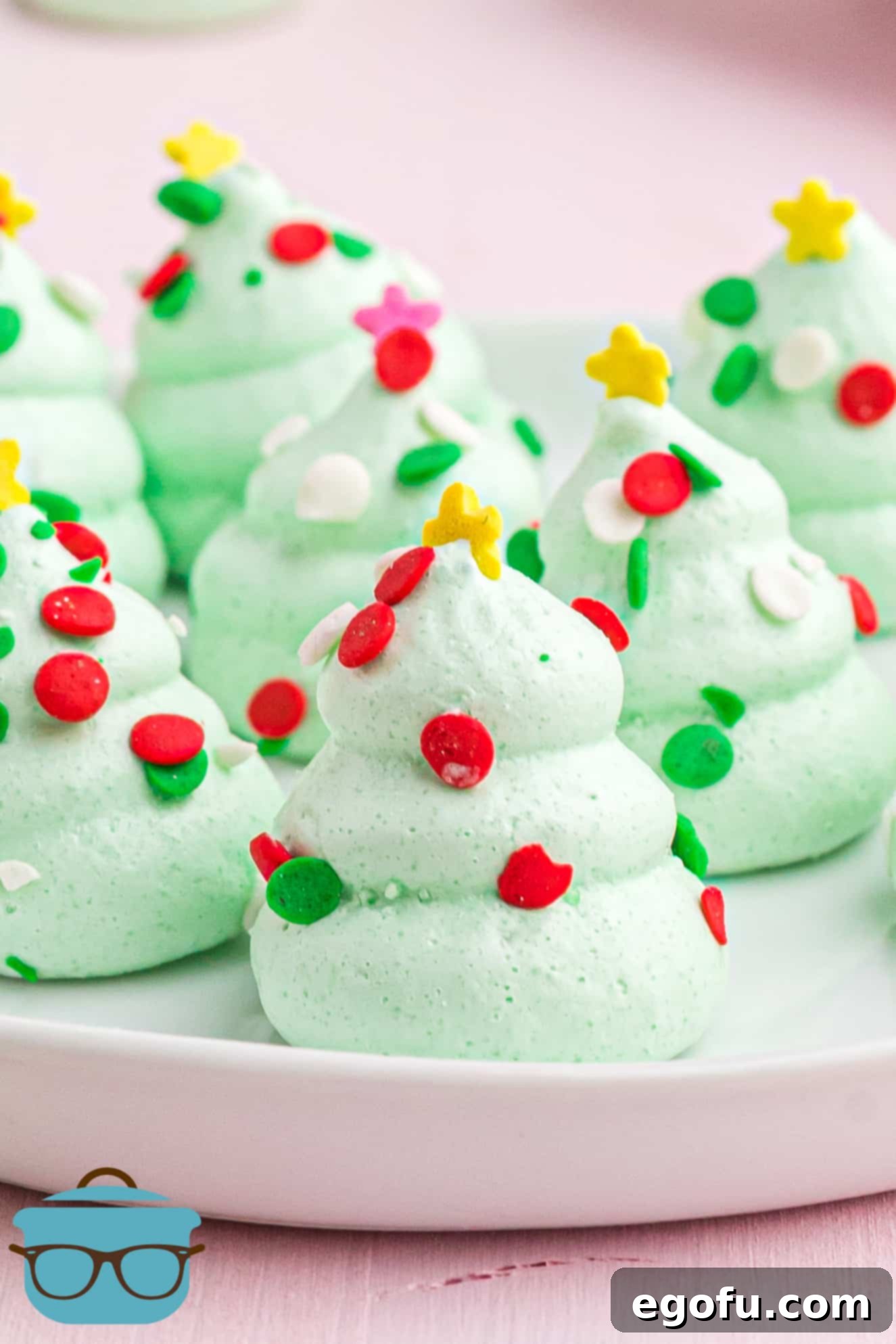 green Christmas tree shaped meringue cookies shown on a small white plate on a pink background.