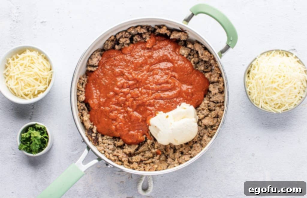 ground sausage and kielbasa in a large skillet with marinara sauce and ricotta cheese on top, ready to be mixed for a cohesive filling