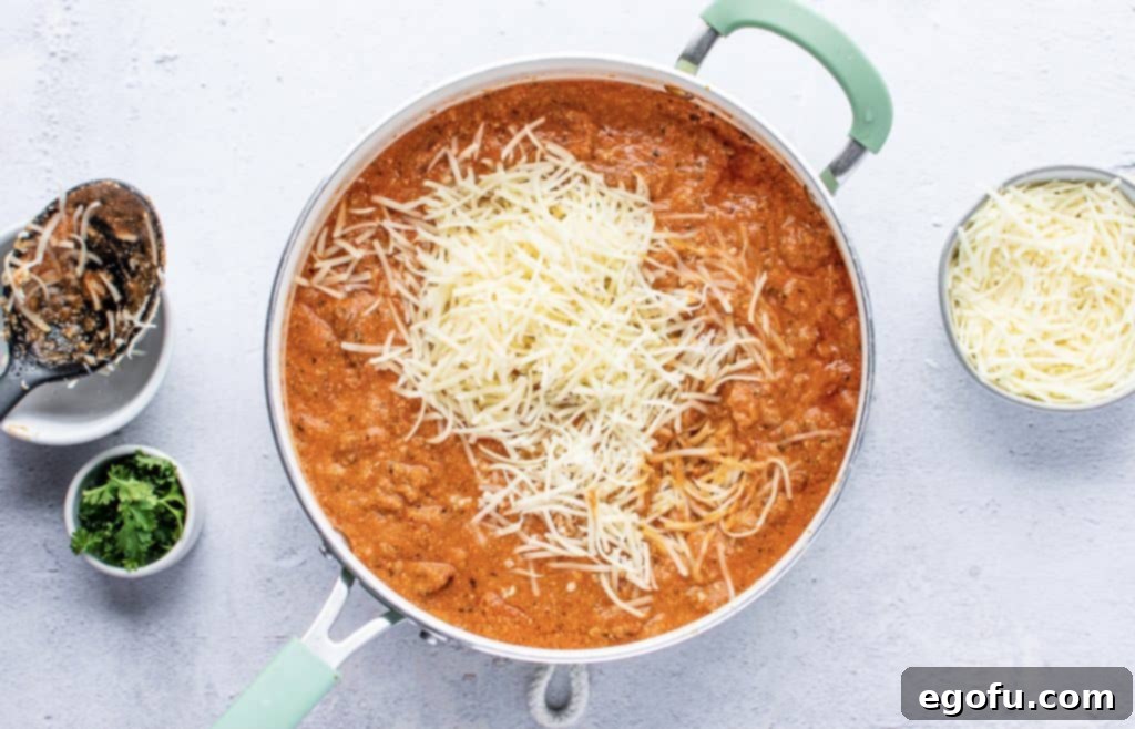 shredded Parmesan and mozzarella cheese on top of Italian sausage sauce in a skillet, awaiting mixture to create a cheesy filling