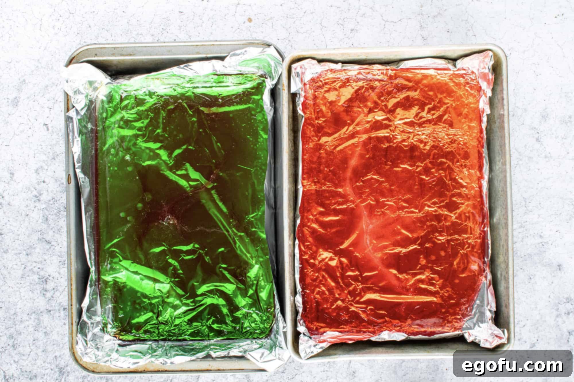 Vibrant red and green liquid rock candy syrups, after flavoring, are carefully poured into two separate baking pans, each lined with aluminum foil.