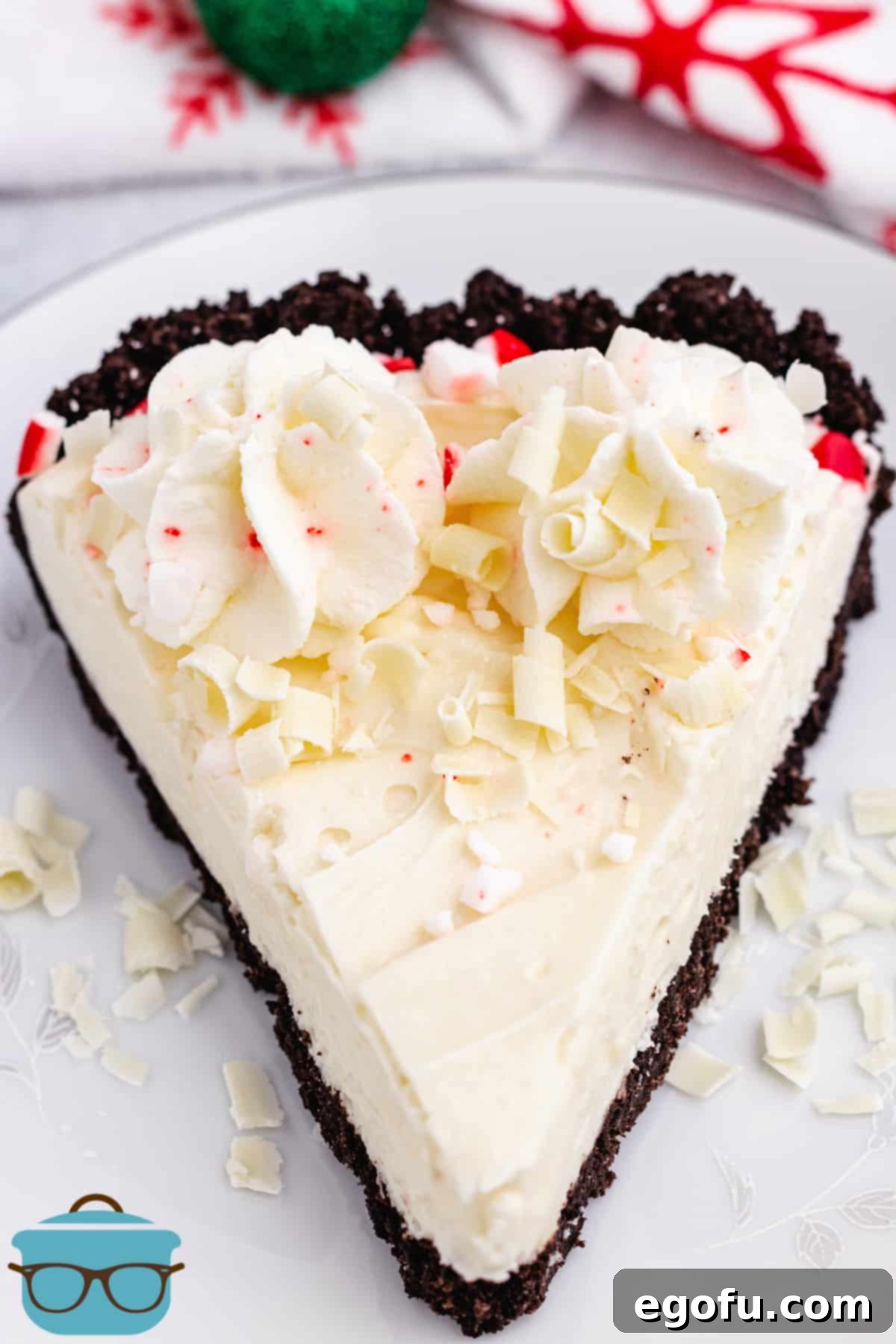 A beautifully presented slice of White Chocolate Peppermint Pie on a white plate, adorned with delicate white chocolate shavings, showcasing its creamy filling and dark crust.