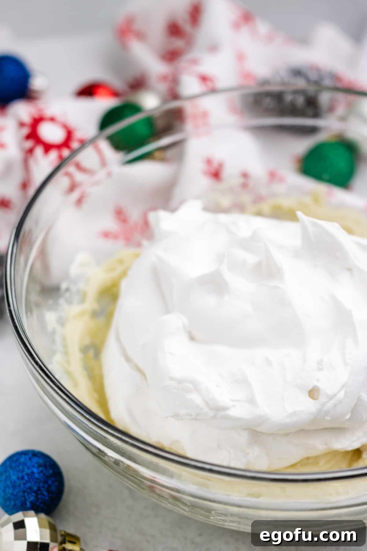 Thawed whipped topping being gently folded into the bowl containing the cream cheese and melted white chocolate mixture for the pie filling.