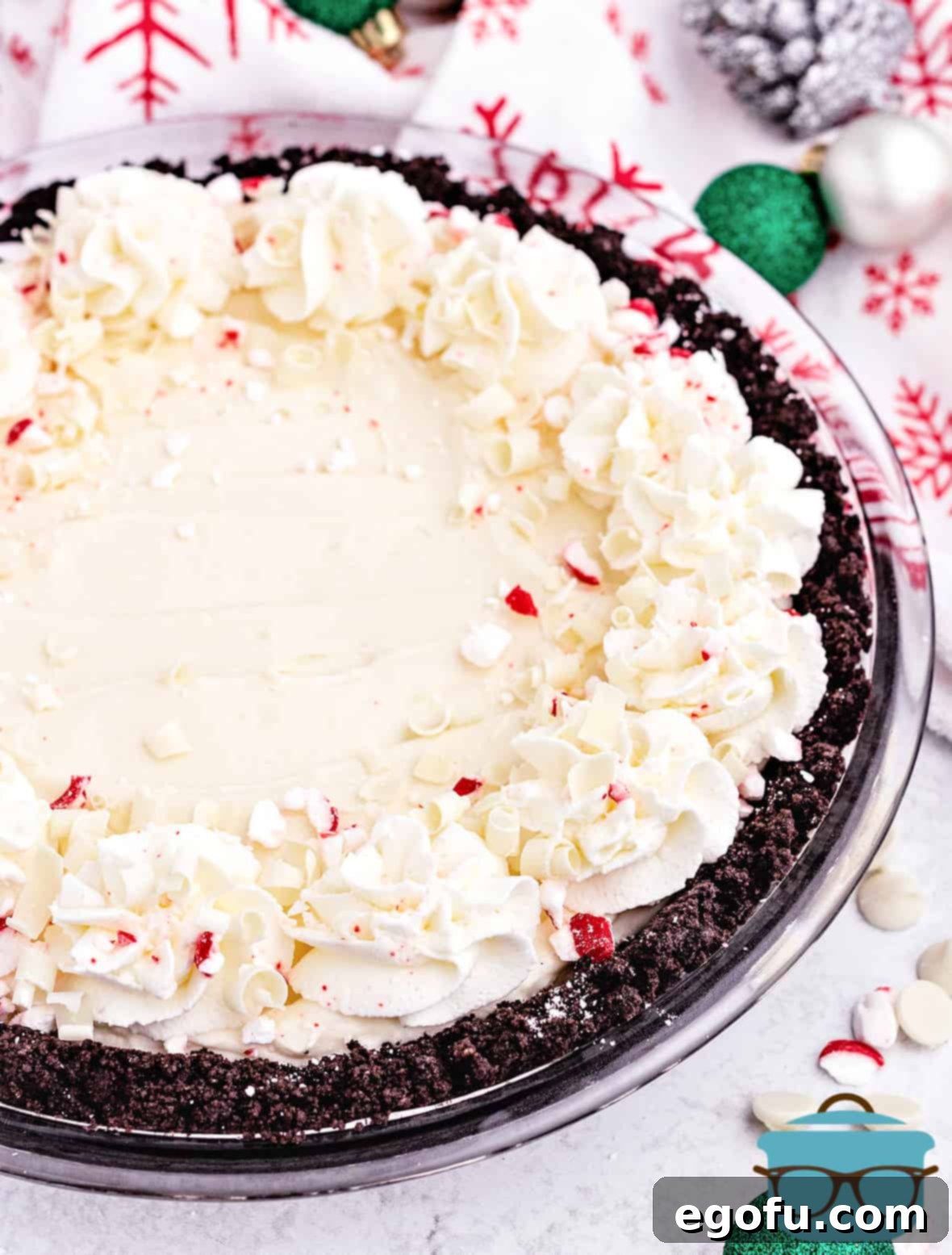 A festive Peppermint Pie with artfully decorated whipped cream edges, adorned with Christmas ornaments in the background, showcasing its holiday presentation.