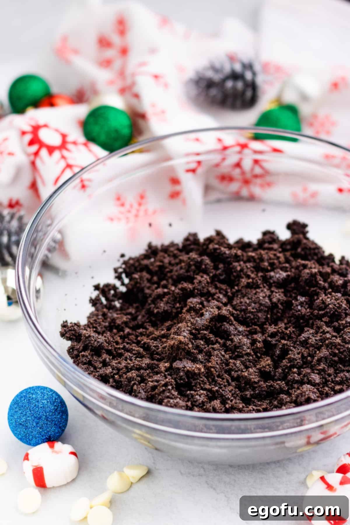 Melted butter being drizzled over crushed Oreo cookies in a clear glass mixing bowl, illustrating the combining step for the pie crust.