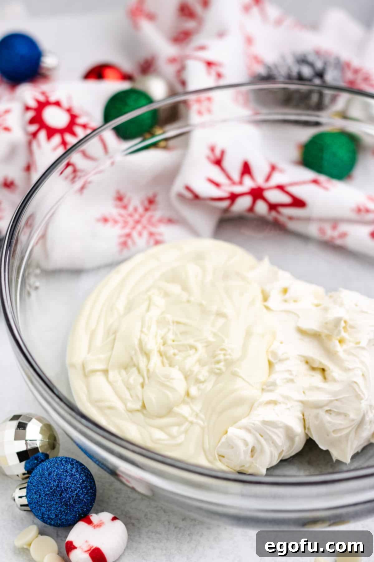 Melted white chocolate and smooth, creamy cream cheese being mixed together in the bottom of a clear mixing bowl, forming the base of the pie filling.