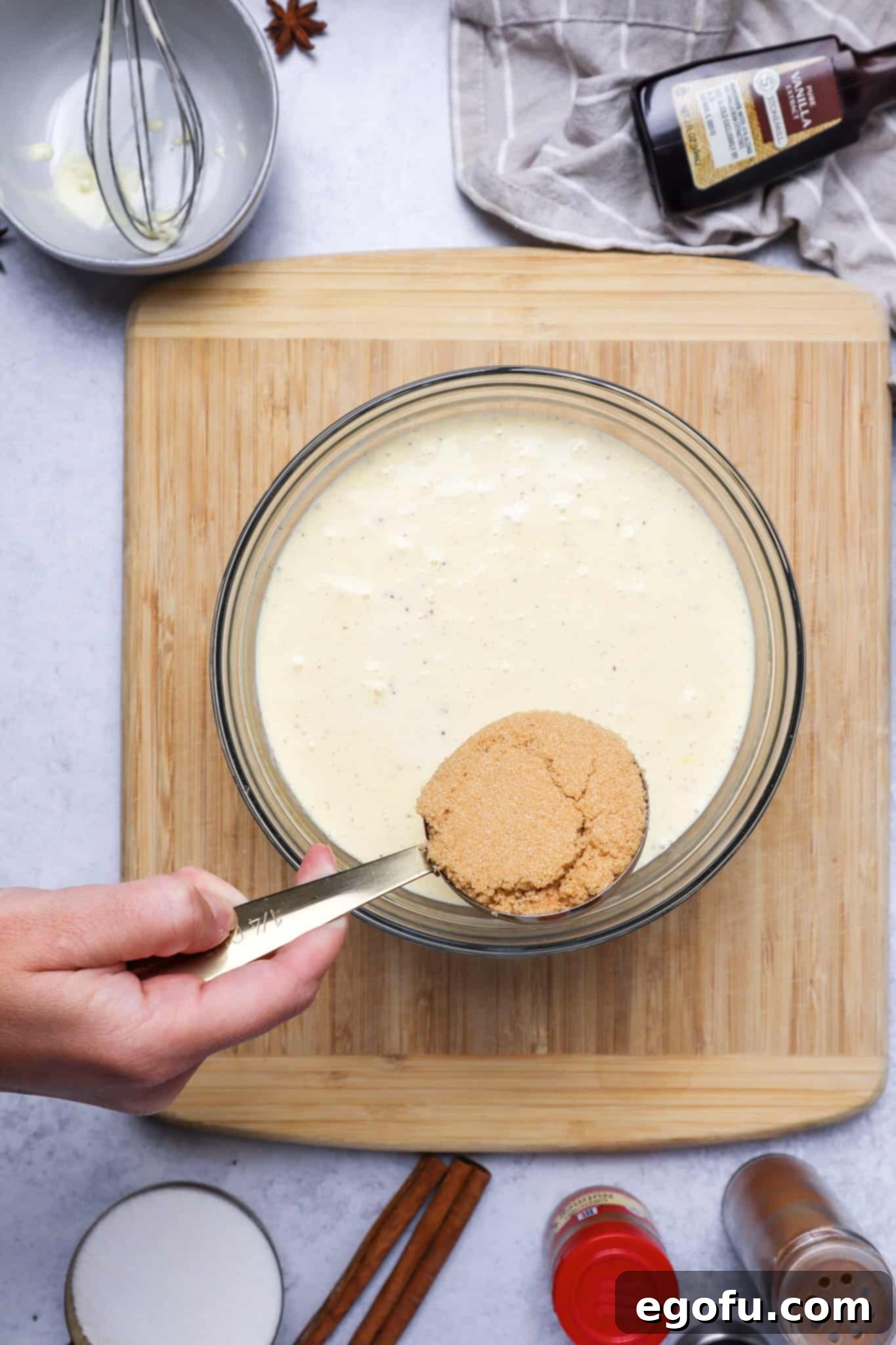 measuring cup filled with brown sugar held over a bowl filled with egg and milk mixture.