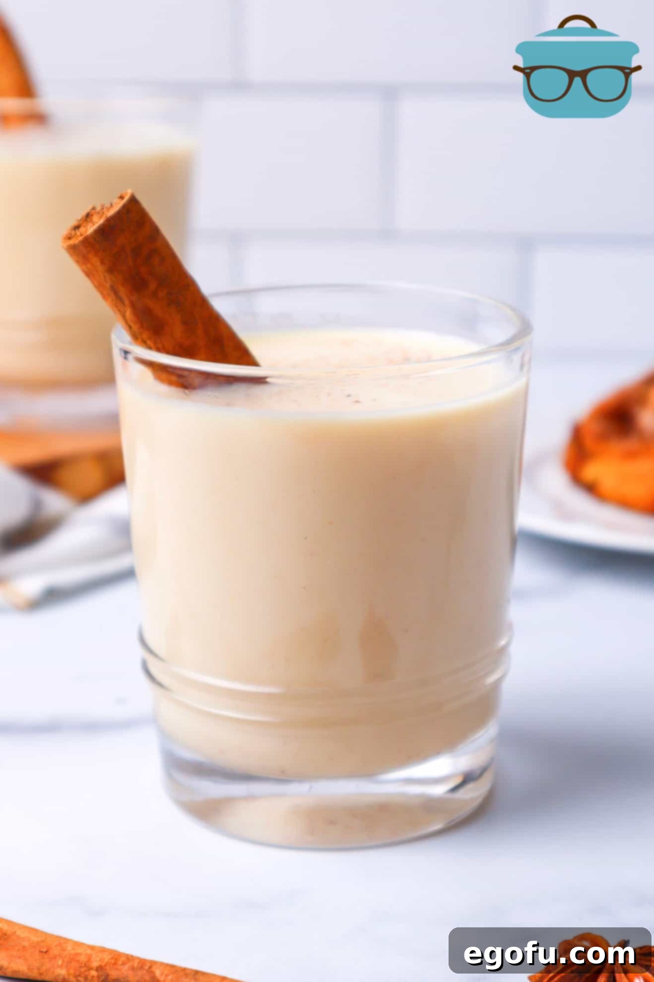 glass of egg nog with cinnamon stick shown in front of a white background.