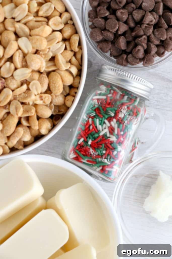 A vibrant flat lay of all the essential ingredients: Vanilla almond bark, salted, roasted peanuts, milk chocolate chips, coconut oil, and a small dish of colorful sprinkles.