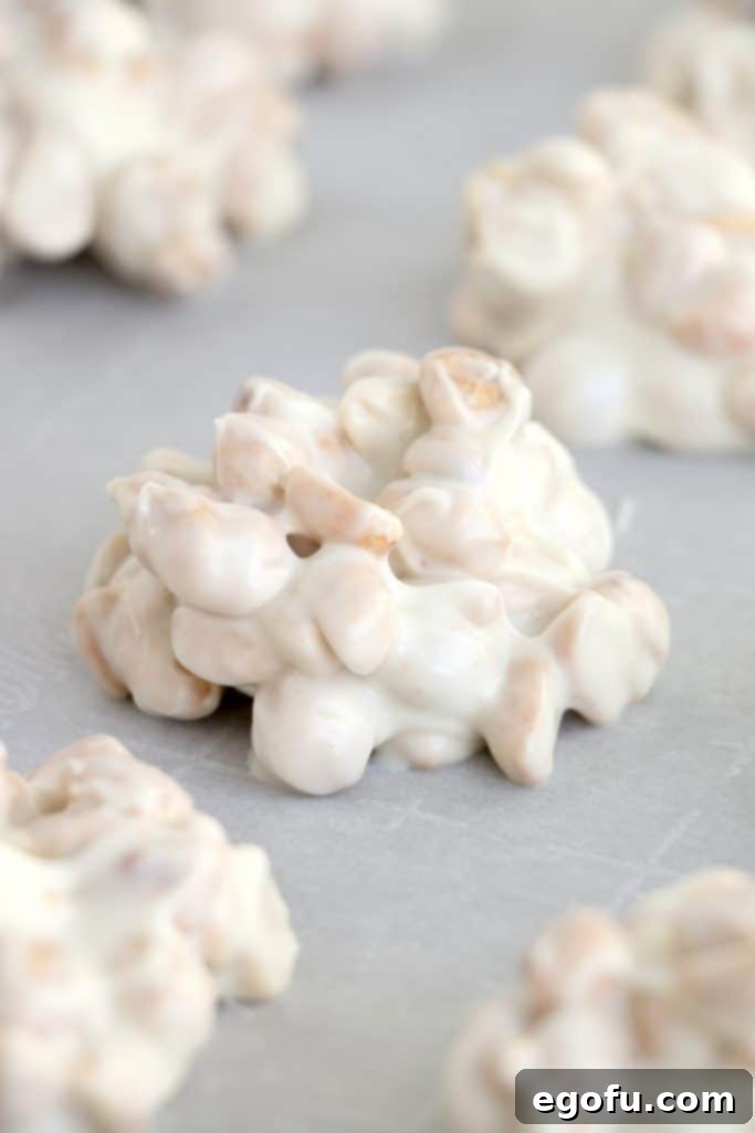 A single white chocolate peanut cluster is shown on parchment paper, firm and ready for the chocolate drizzle.