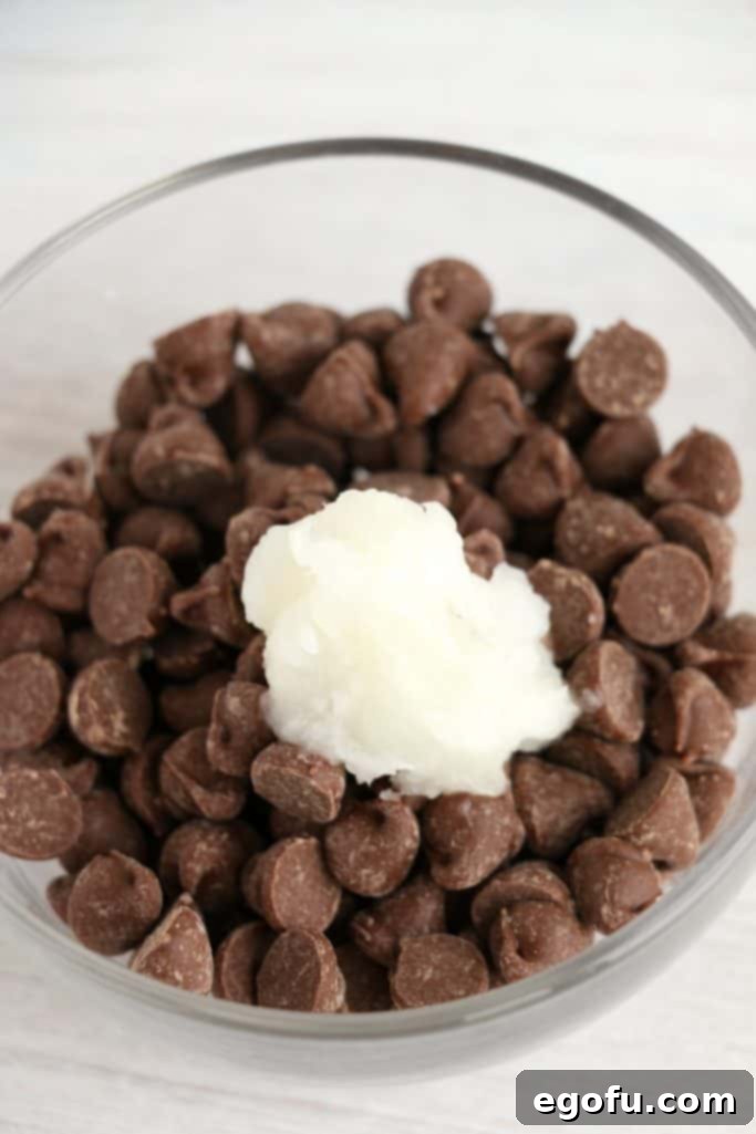 Milk chocolate chips and coconut oil nestled in a small clear bowl, prepared for melting to create the perfect drizzle.