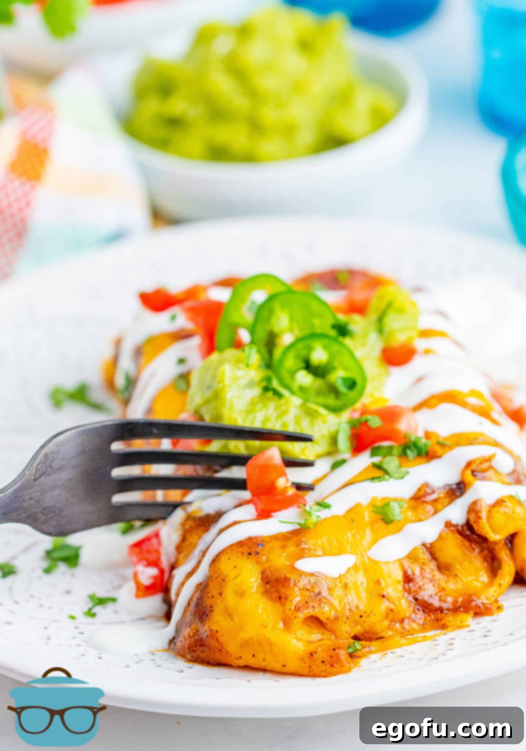 Two enchiladas on a white plate with a fork slicing through one of the enchiladas, revealing the succulent filling.