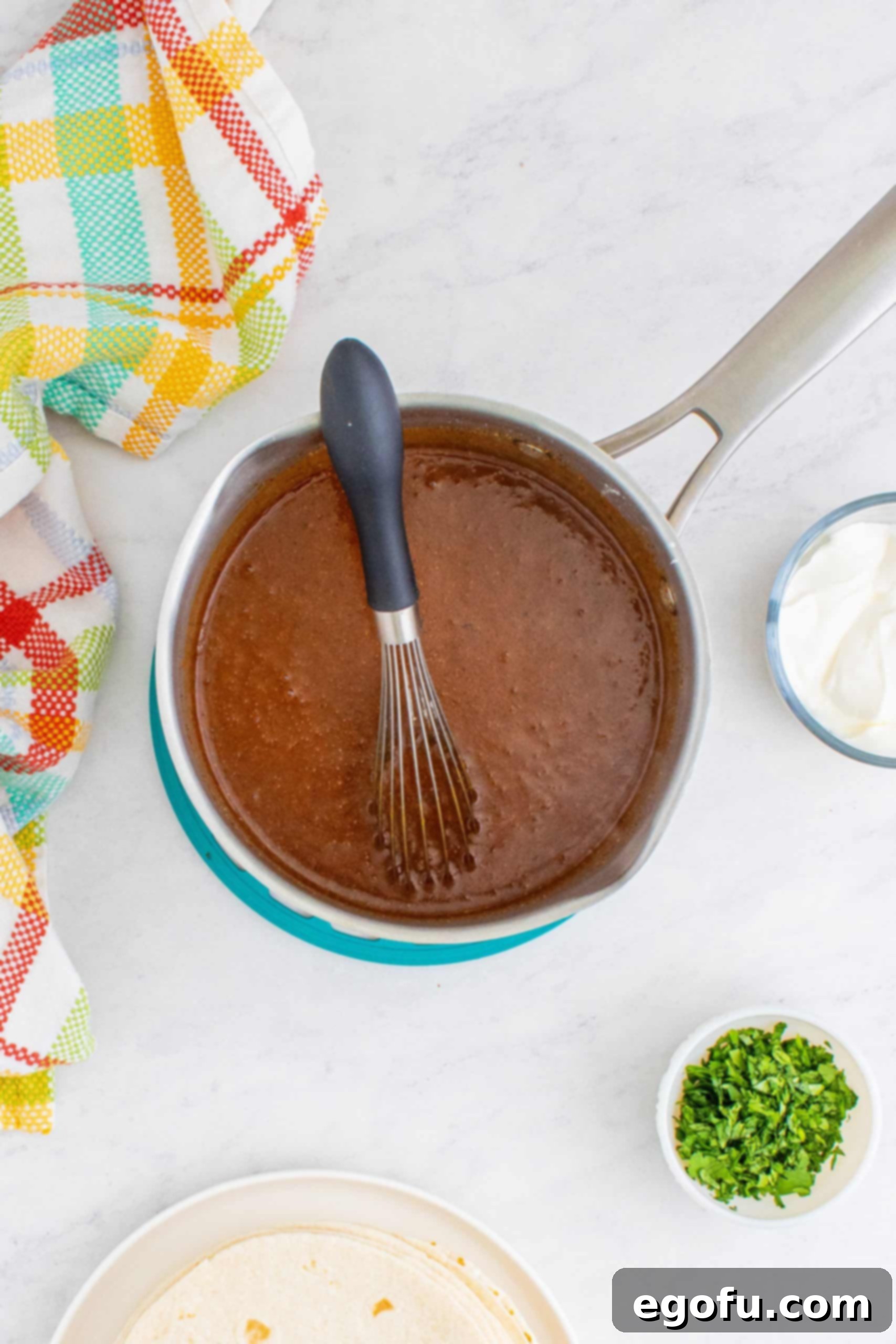 Homemade Enchilada Red Sauce shown in a sauce pot with a whisk, demonstrating the smooth texture.