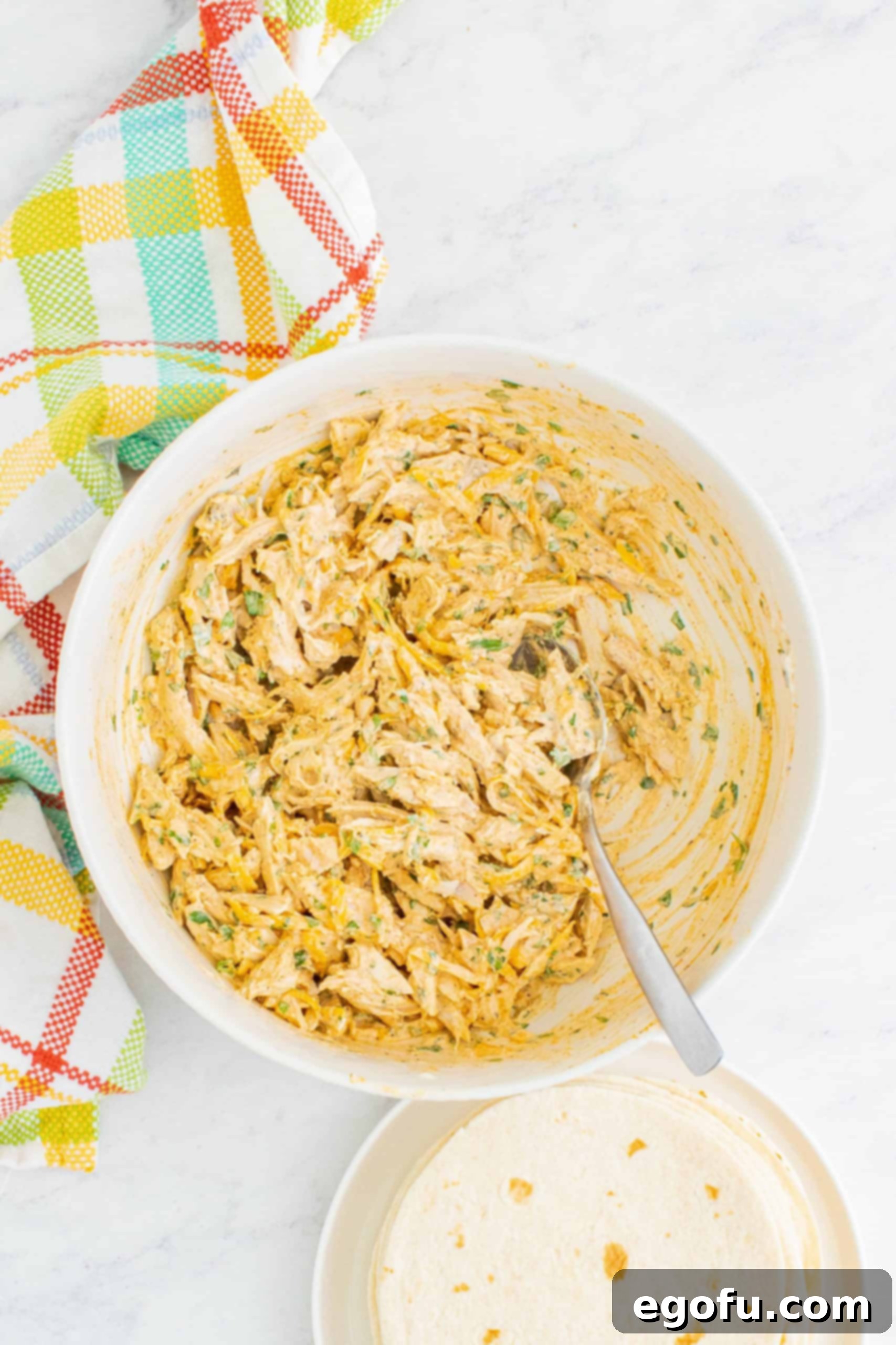Shredded chicken, sour cream, cheddar cheese, and cilantro shown mixed together in a large white bowl, ready for filling.